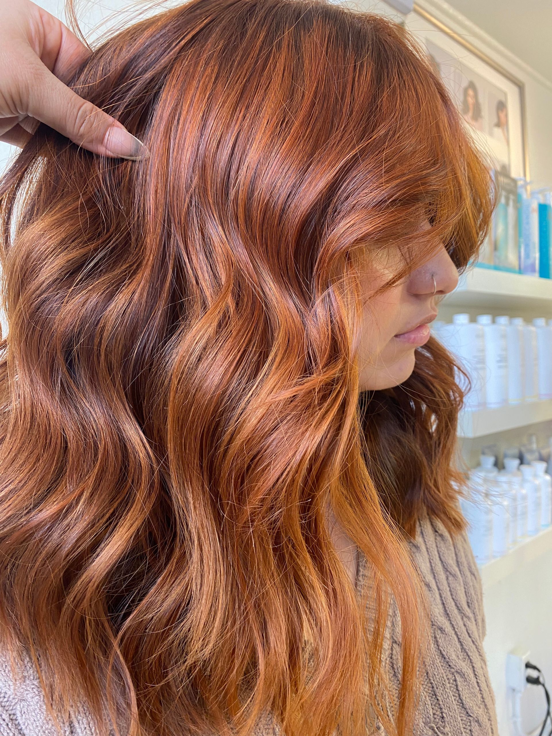 A woman with long red hair is getting her hair dyed in a salon.