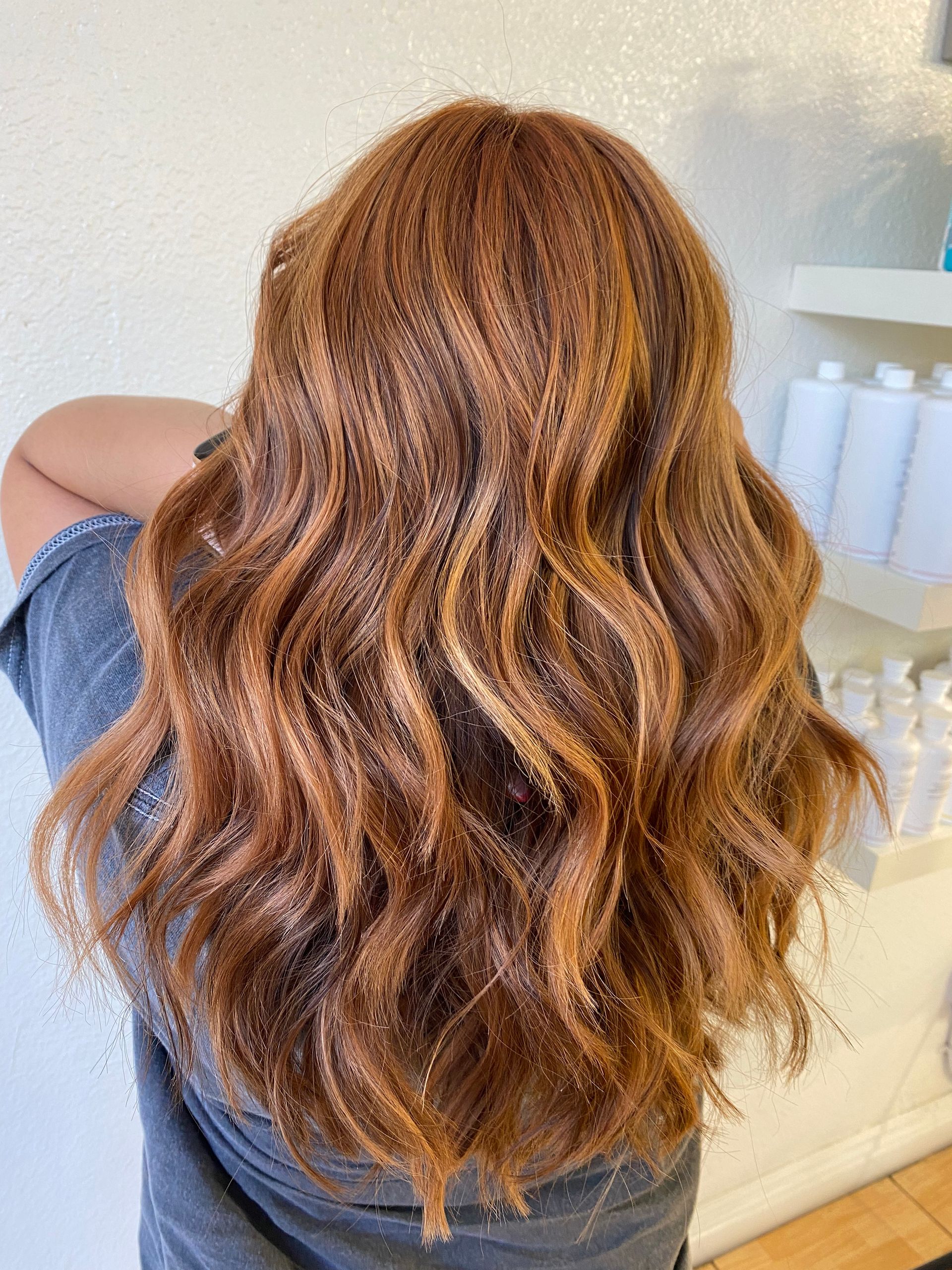 A woman with long brown hair is standing in front of a shelf with bottles of hair products.