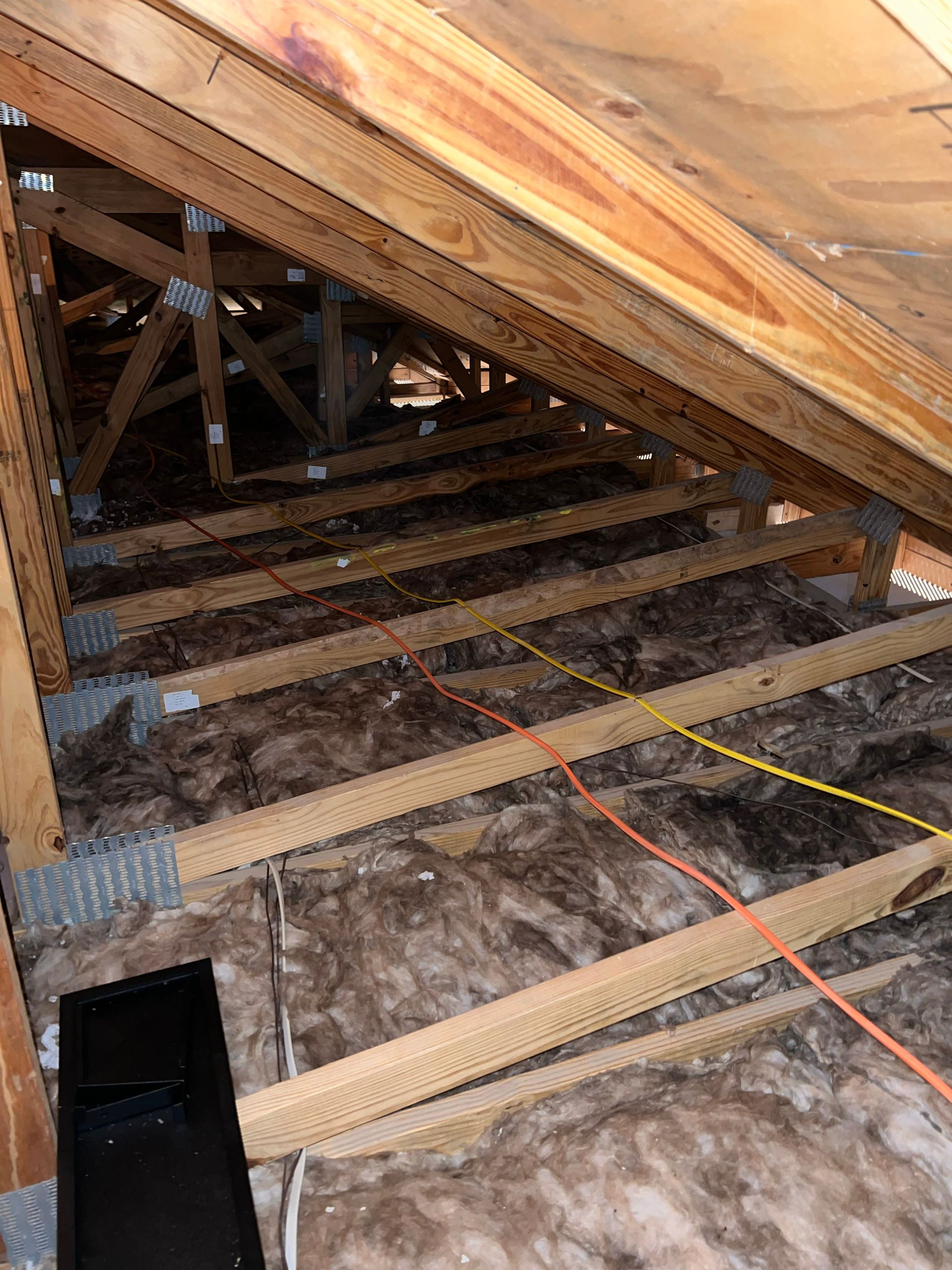 The ceiling of an attic with wooden beams and insulation.