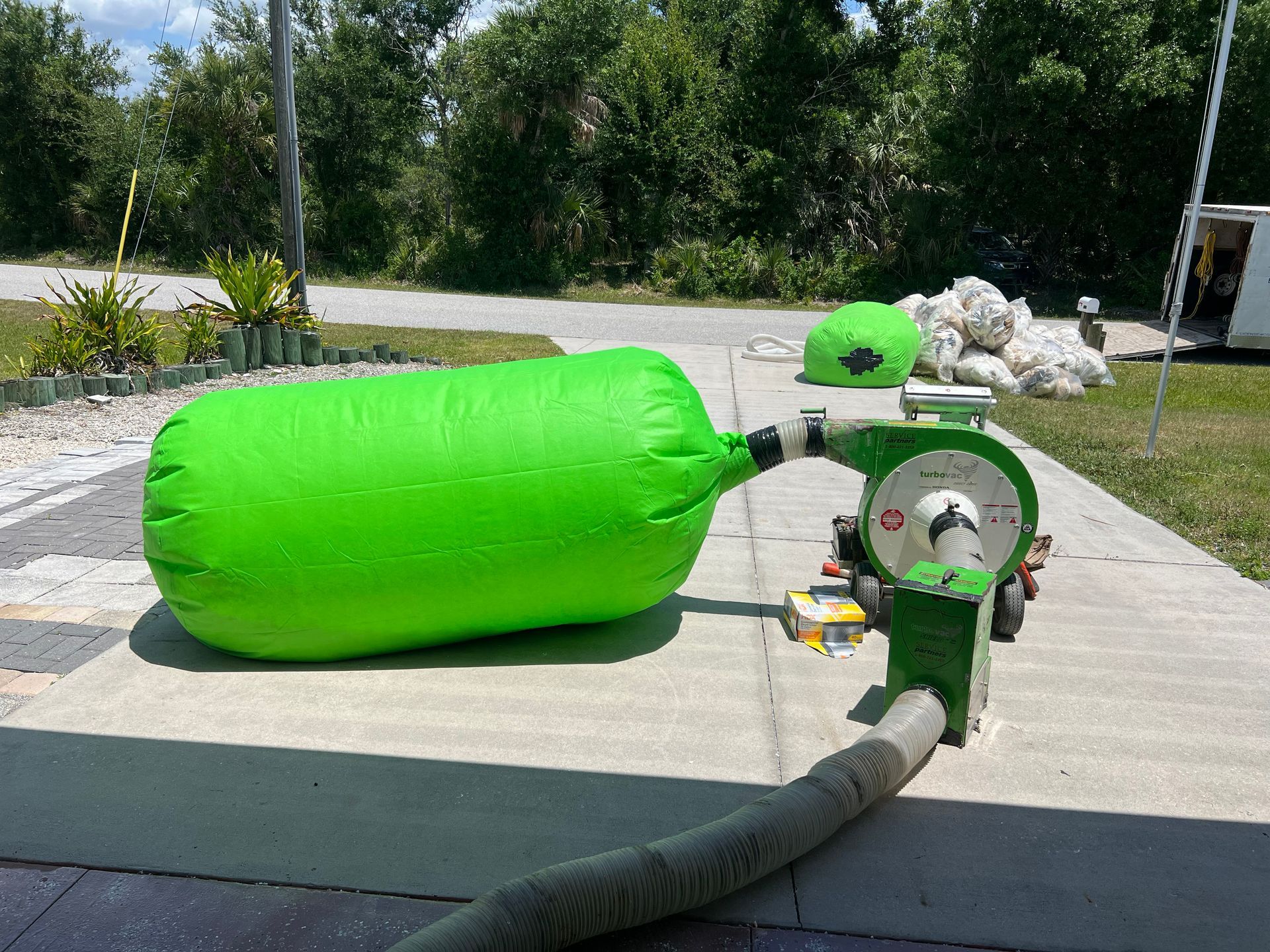 A green bag with a hose attached to it is sitting on a sidewalk.