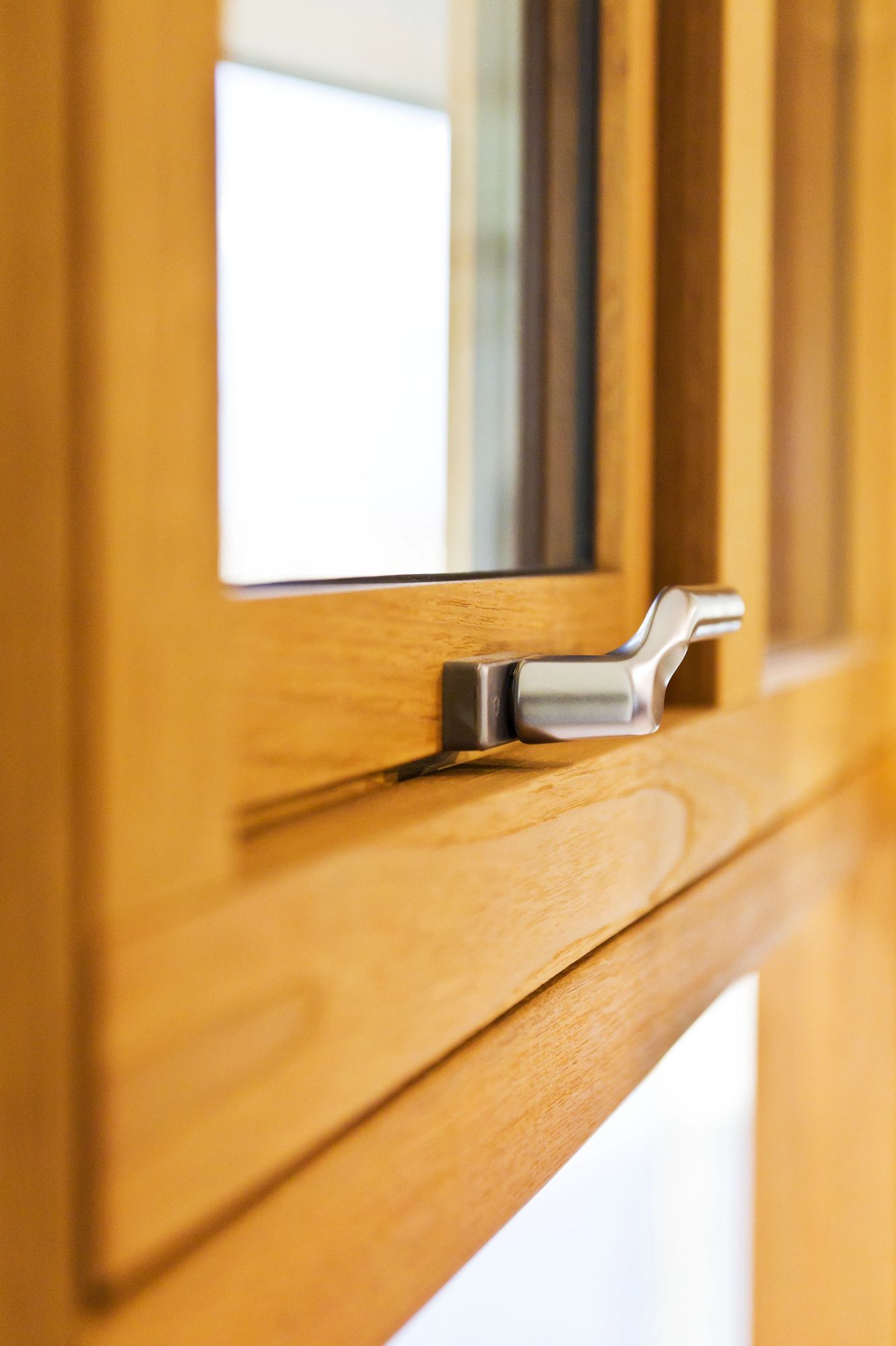 Primo piano del telaio di una finestra in legno con maniglia a leva argentata.