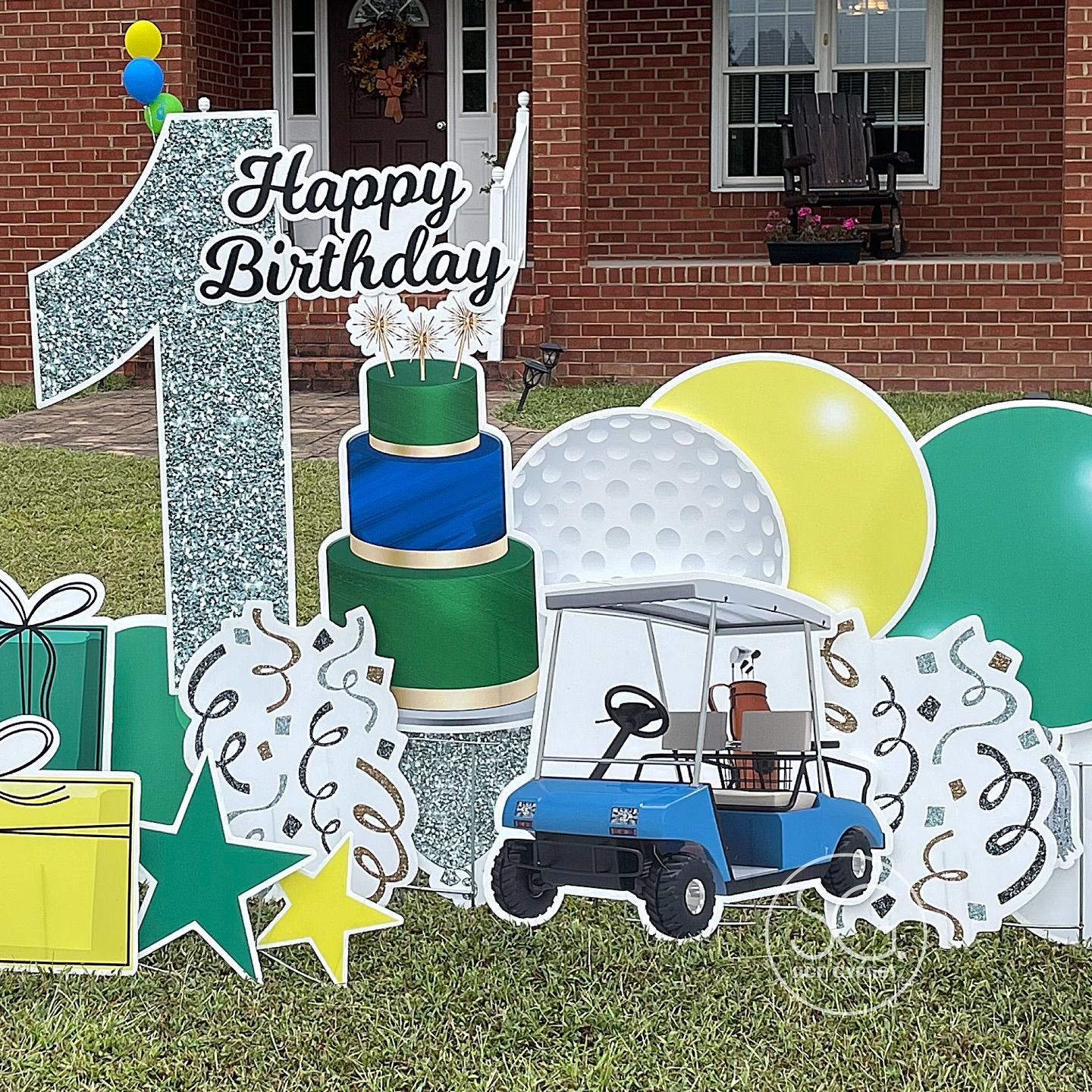 A yard sign for a first birthday with a cake , golf cart , balloons , and gifts.