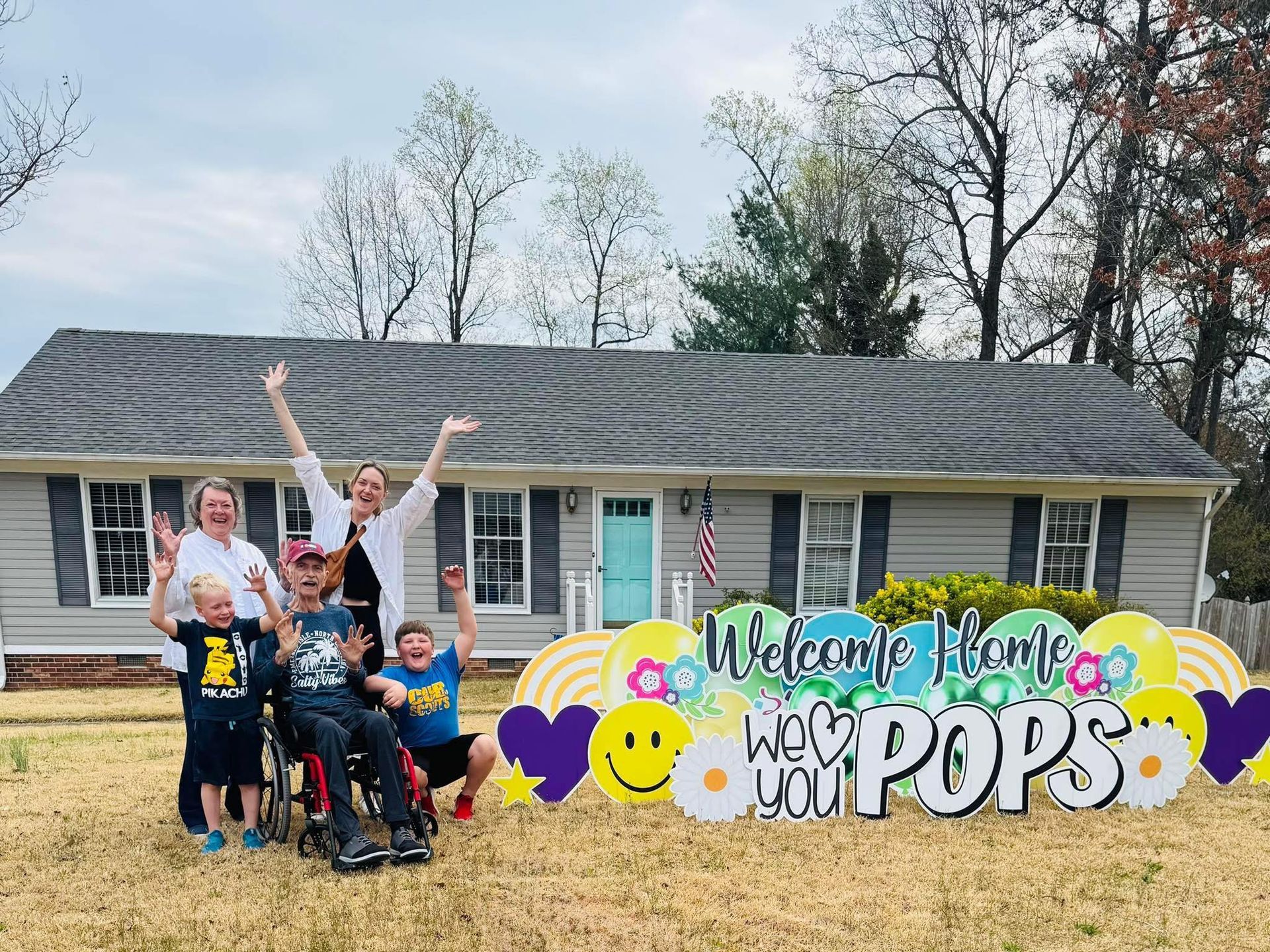 A family is standing in front of a house with a welcome home sign.