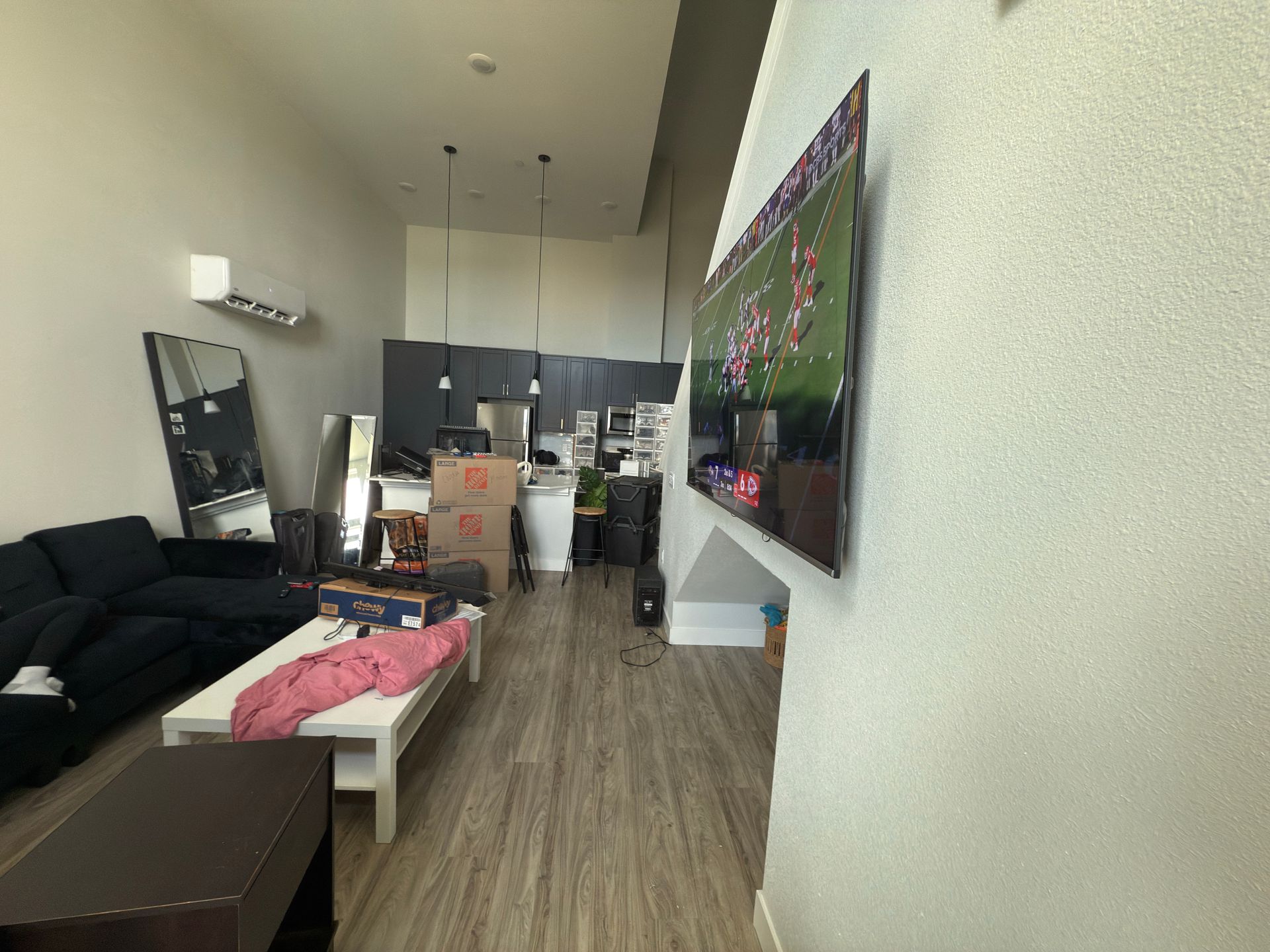 A wide-angle shot of a modern living room featuring a dark sofa, white coffee table, and a wall-mounted TV.