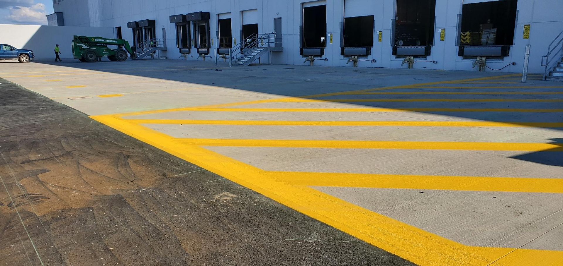 A parking lot with yellow lines painted on it in front of a warehouse.