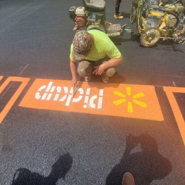 A man is kneeling down to paint a sign on the ground.