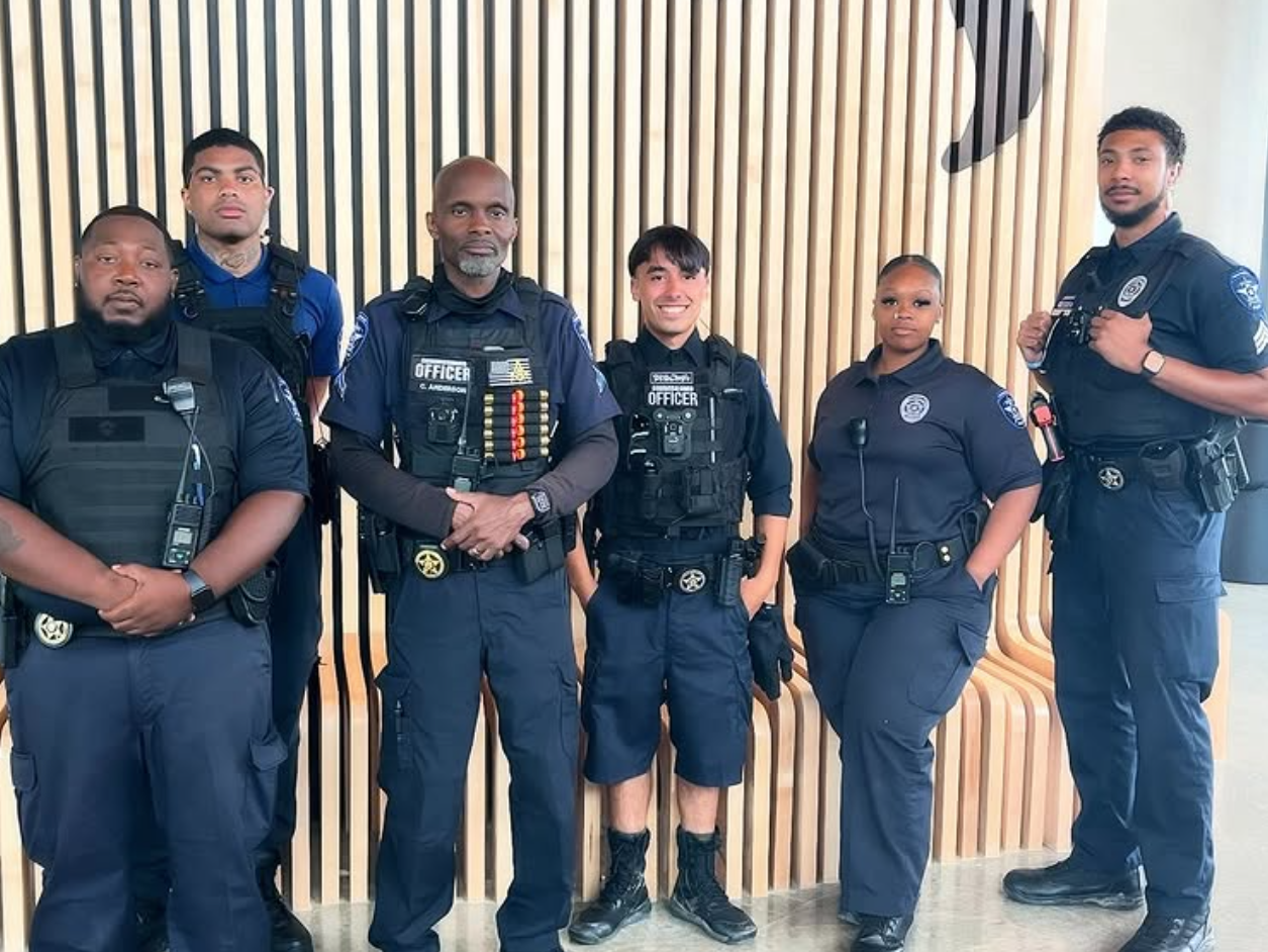 Group of police officers, in uniform, posing in front of wooden slats.
