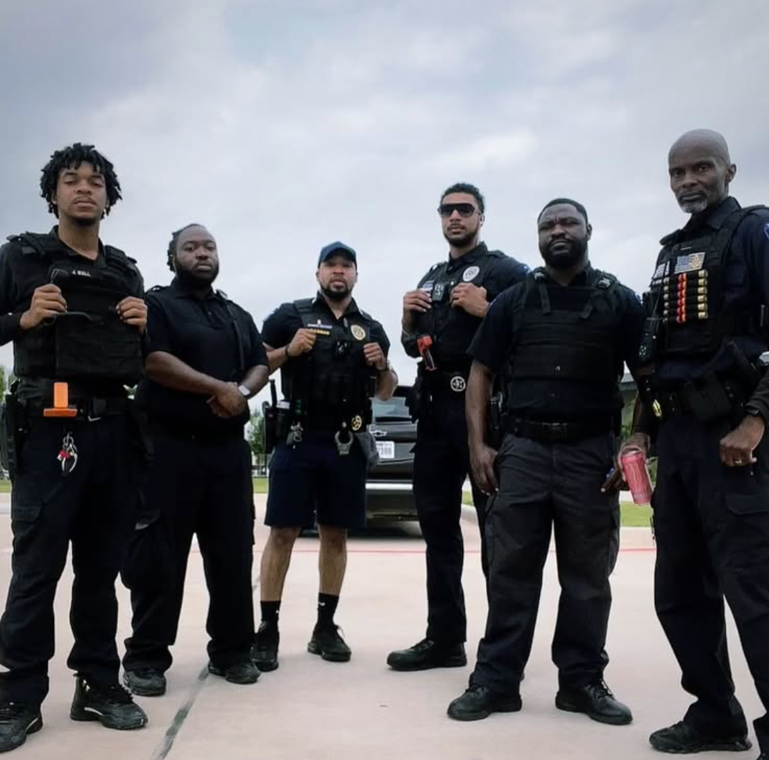 Group of six Black police officers in uniform stand outdoors.