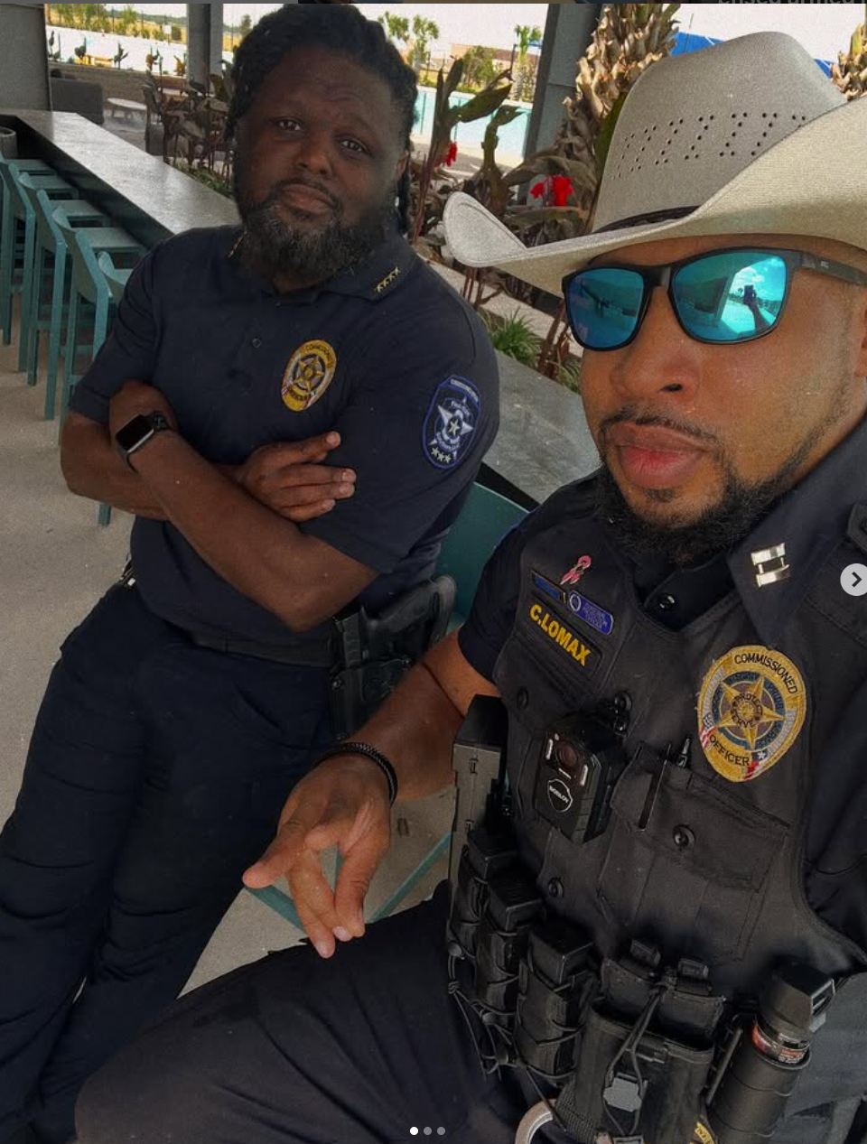 Two police officers posing for a photo, one in a cowboy hat, the other with a beard. Outdoors, sunny.