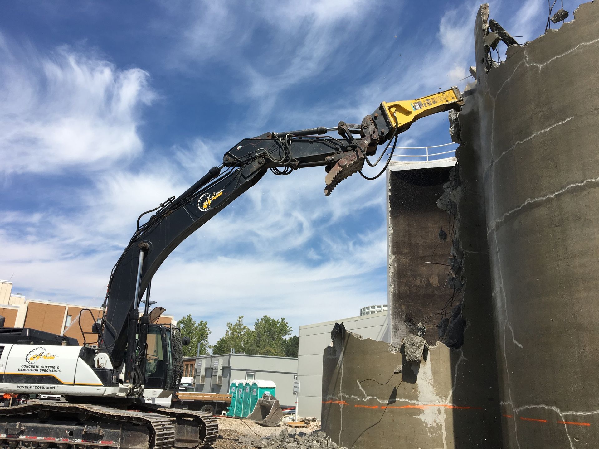 A large excavator with a demolition head breaking down a concrete structure. Blue sky in background.