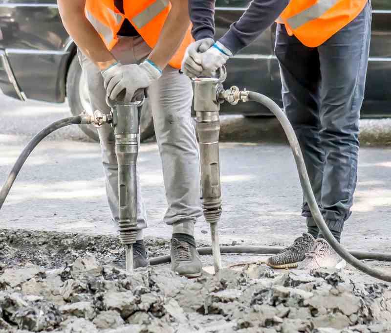 Two construction workers are using a jackhammer to drill a hole in the ground.