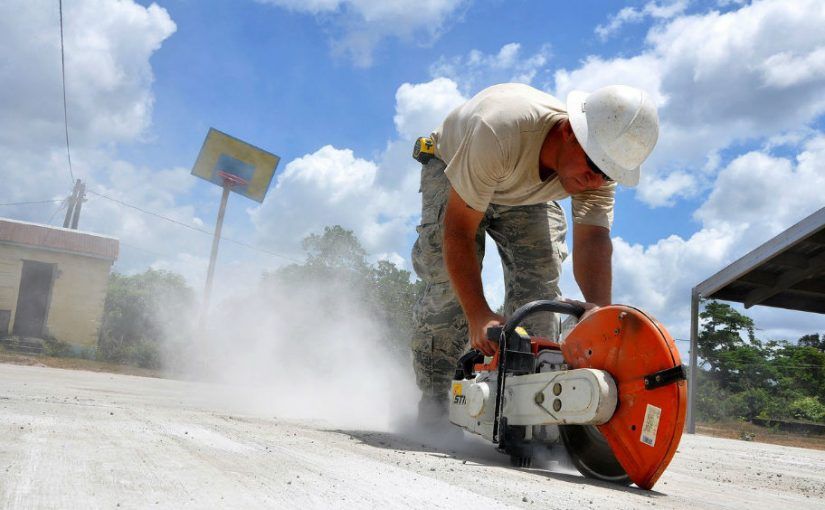 A man wearing a hard hat is cutting concrete with a saw.