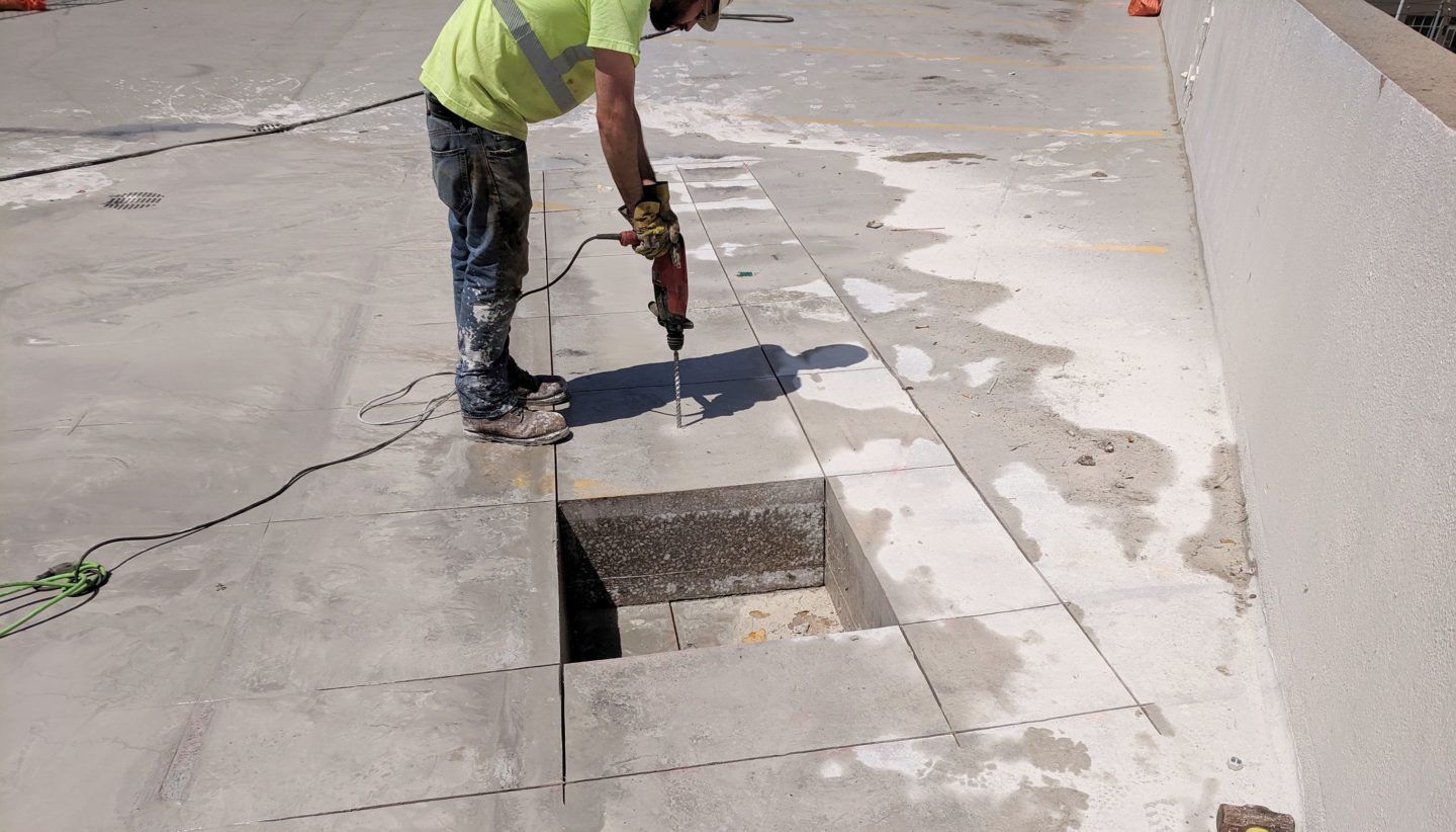 A man is using a drill to cut a hole in the concrete.