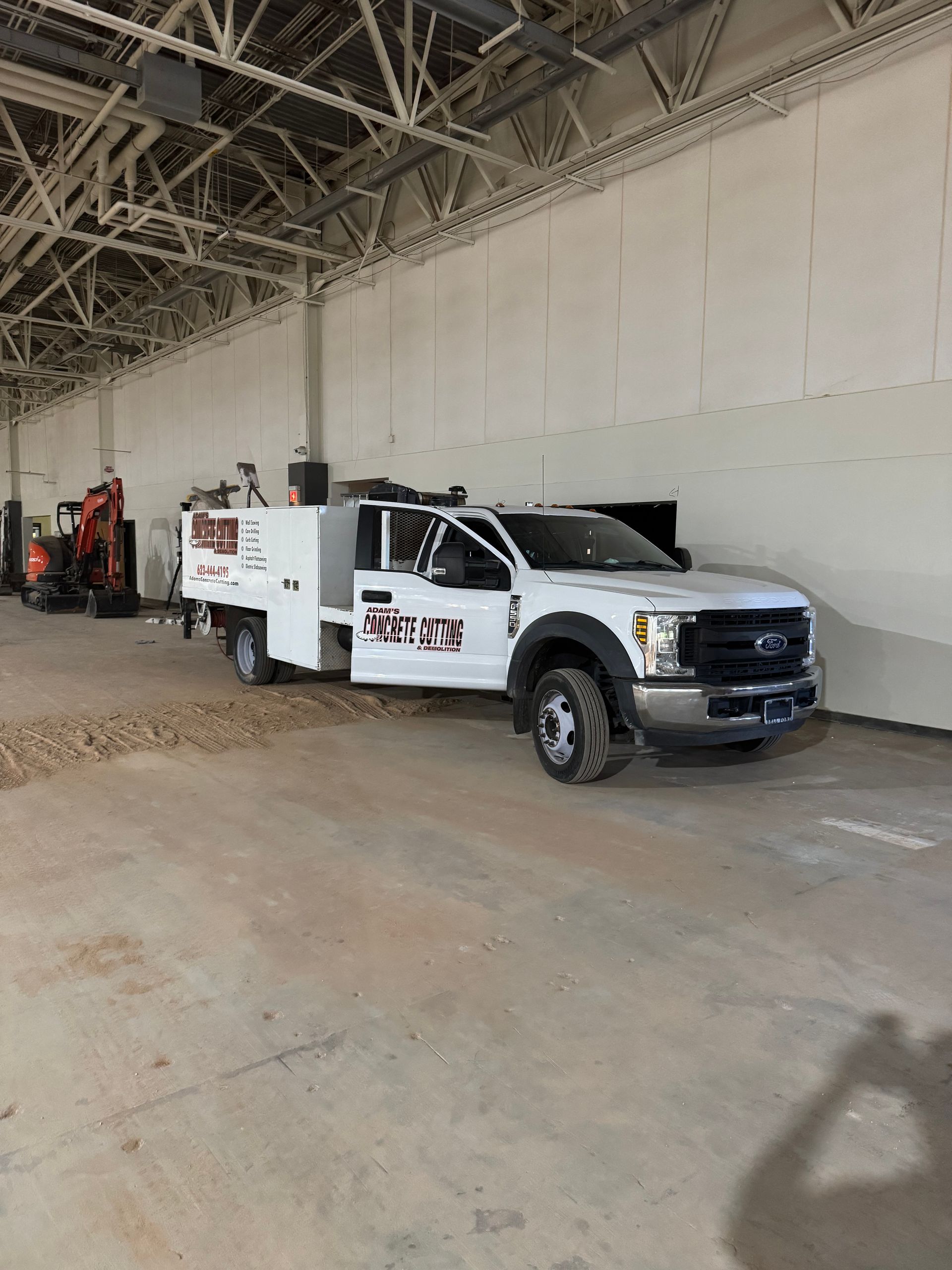 White work truck in a large indoor space, door open, with machinery visible.