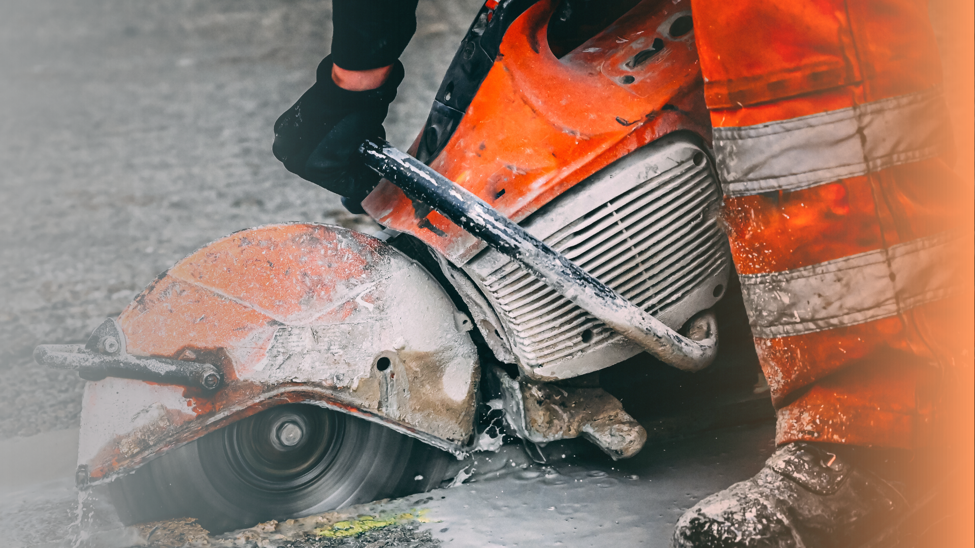 Construction worker in orange overalls using a circular saw to cut concrete.
