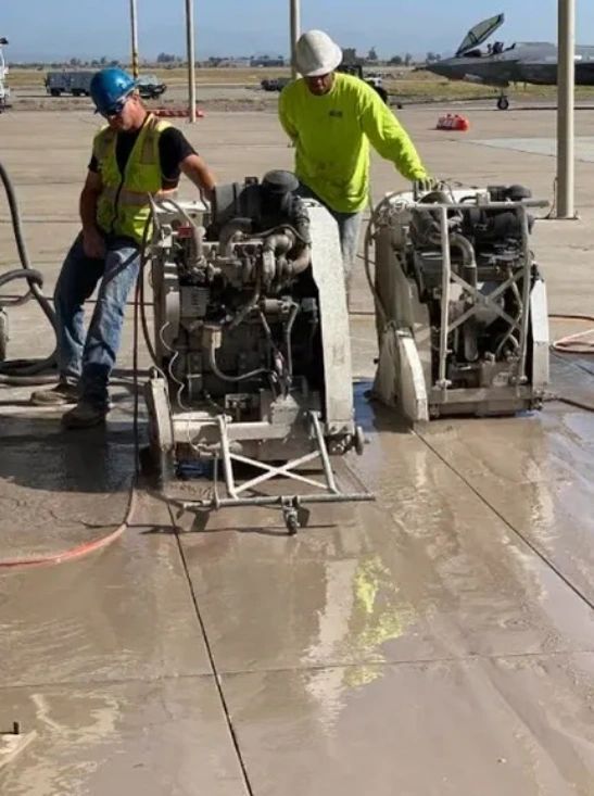 Two men are cutting a concrete floor with a machine.