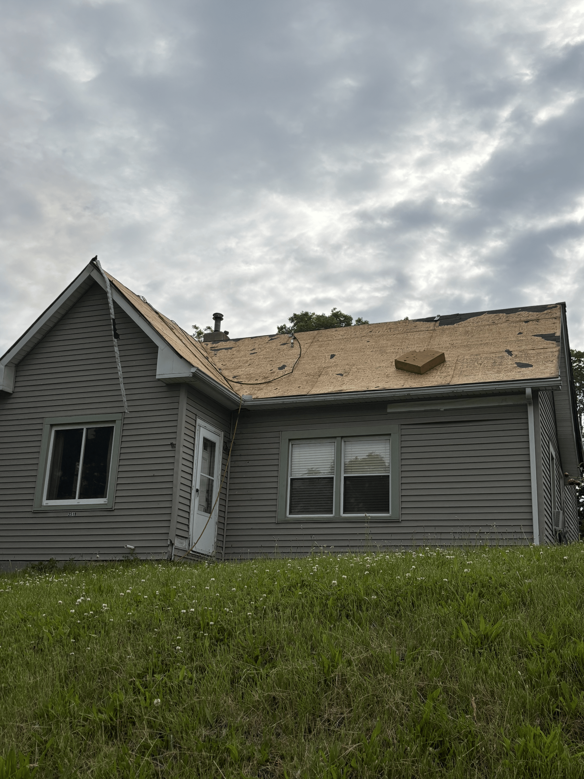 A house with a roof that is missing is sitting on top of a lush green field.