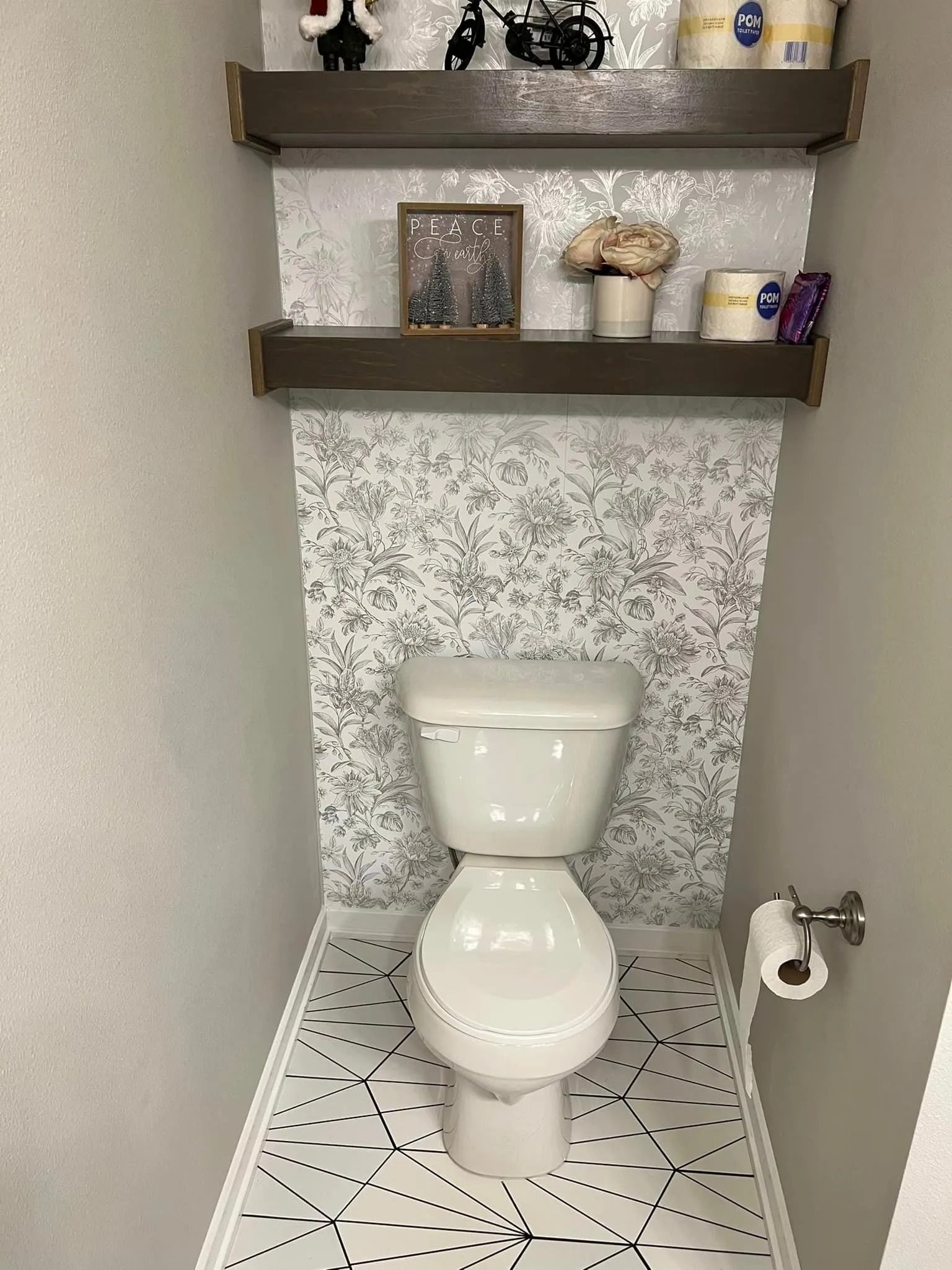 A toilet is sitting in a small bathroom next to a shelf.