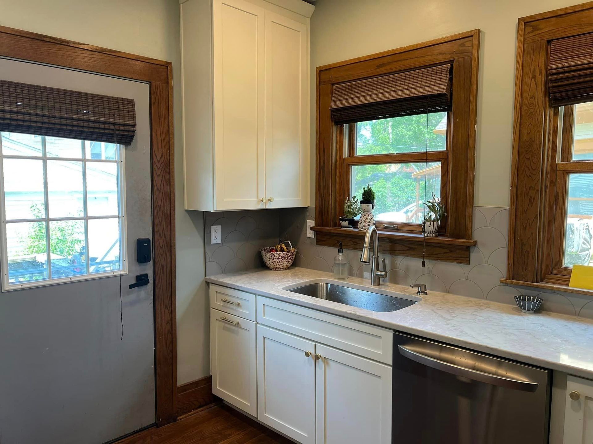 A kitchen with white cabinets , a sink , a dishwasher and a window.
