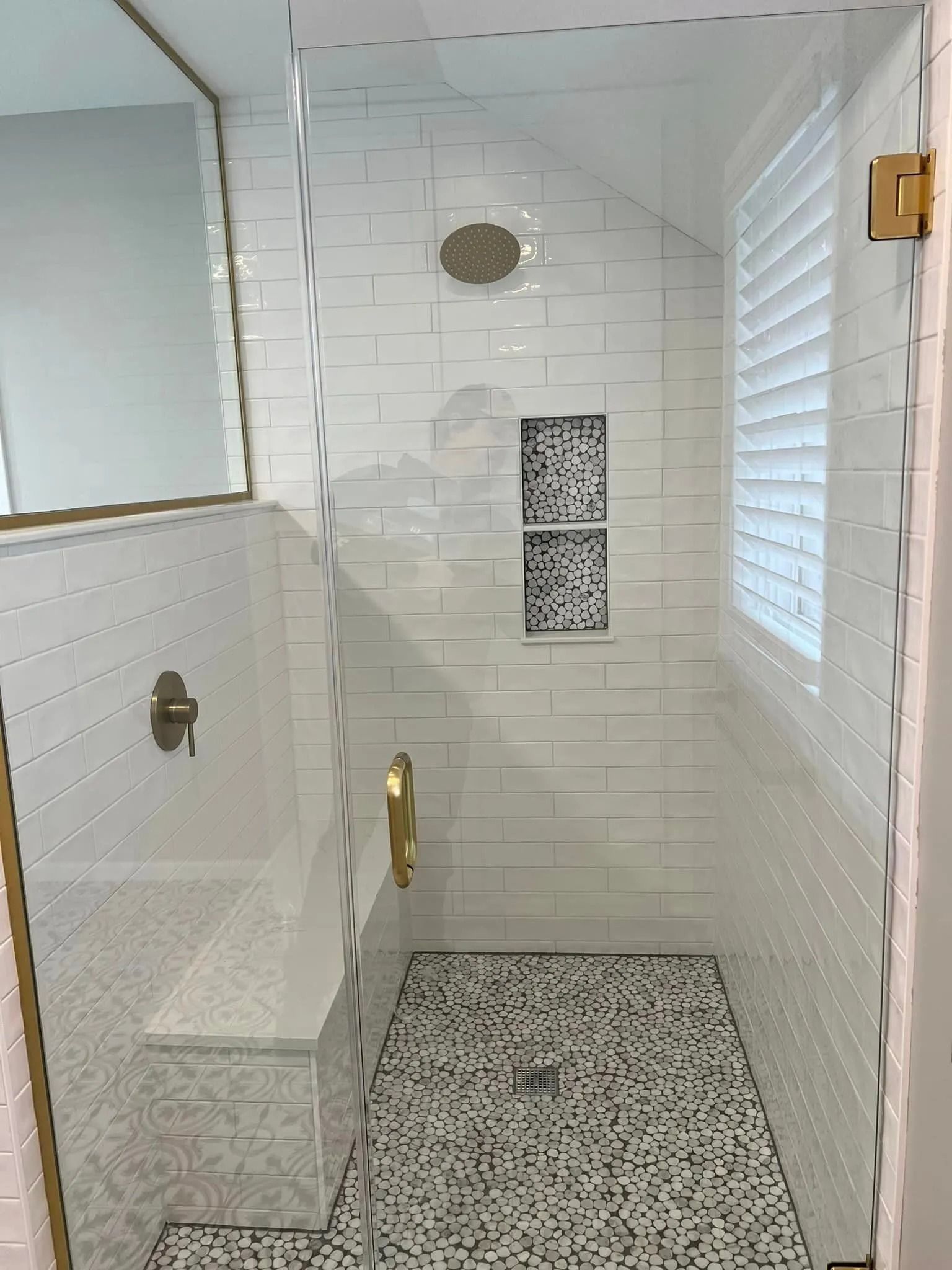 A bathroom with white tiles and a walk in shower with a glass door.
