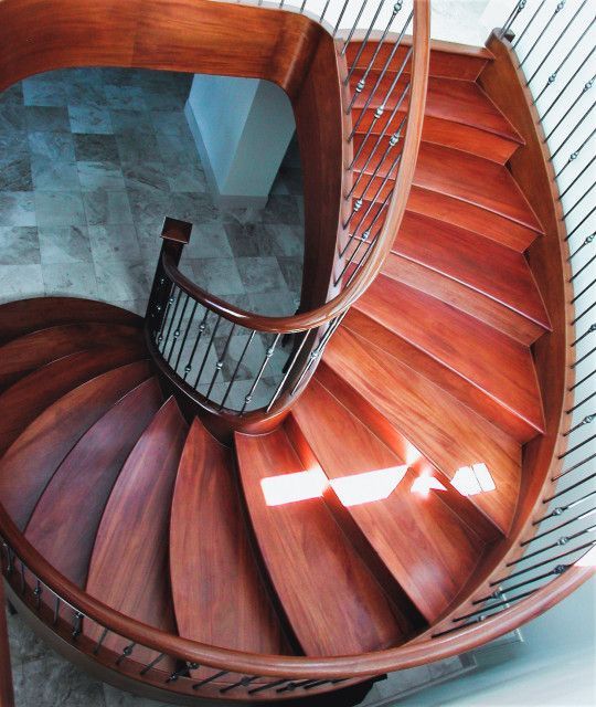 Wooden spiral staircase with polished wood steps, a dark wooden handrail, and a wrought-iron balustrade.