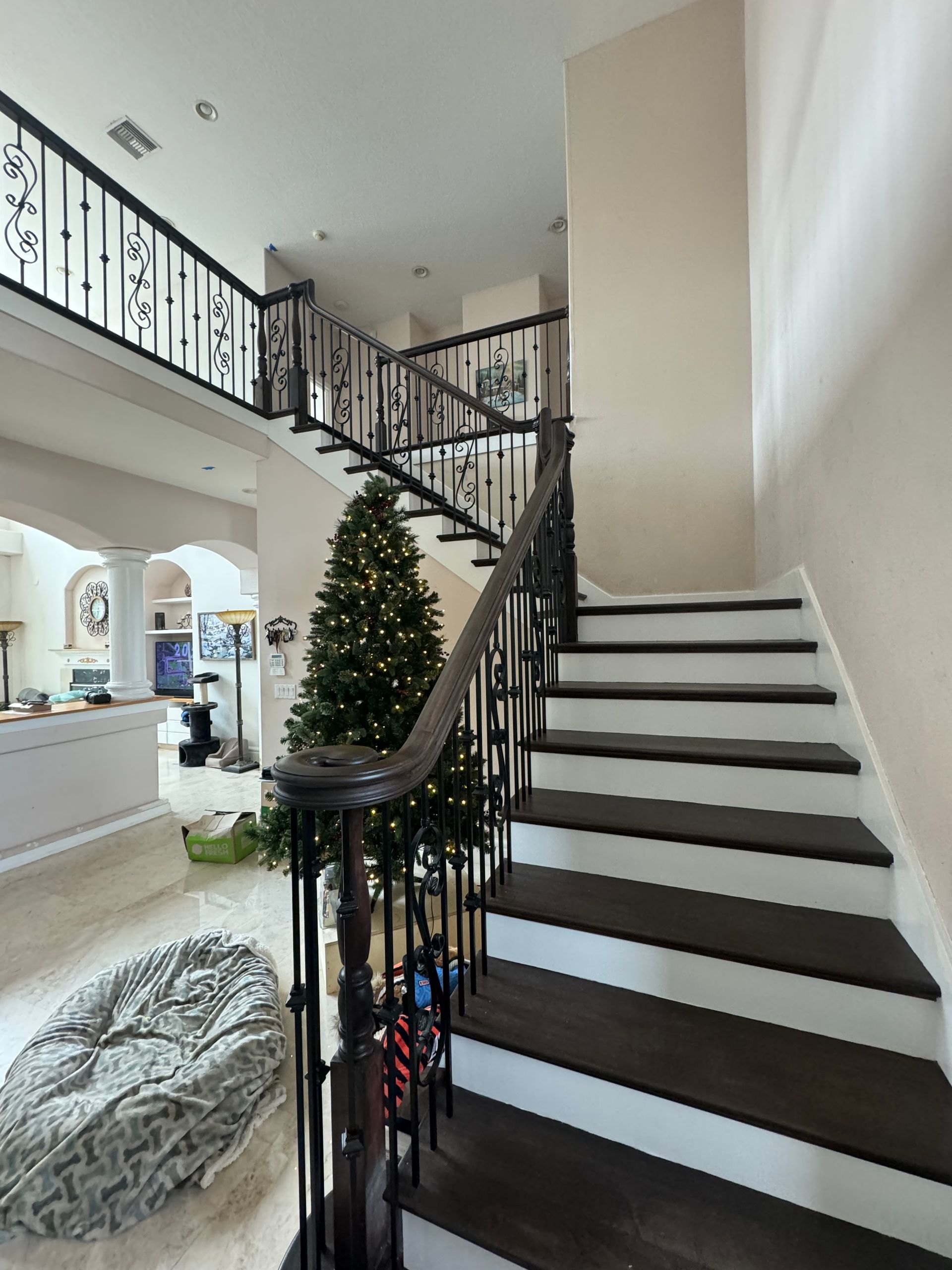 A staircase in a house with a christmas tree in the background.