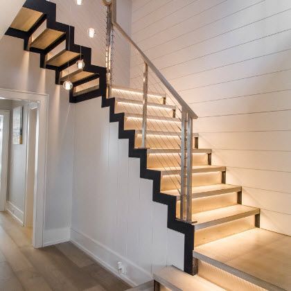 Modern floating staircase with LED lights, steel cable railing, and light wood steps, against white wall.