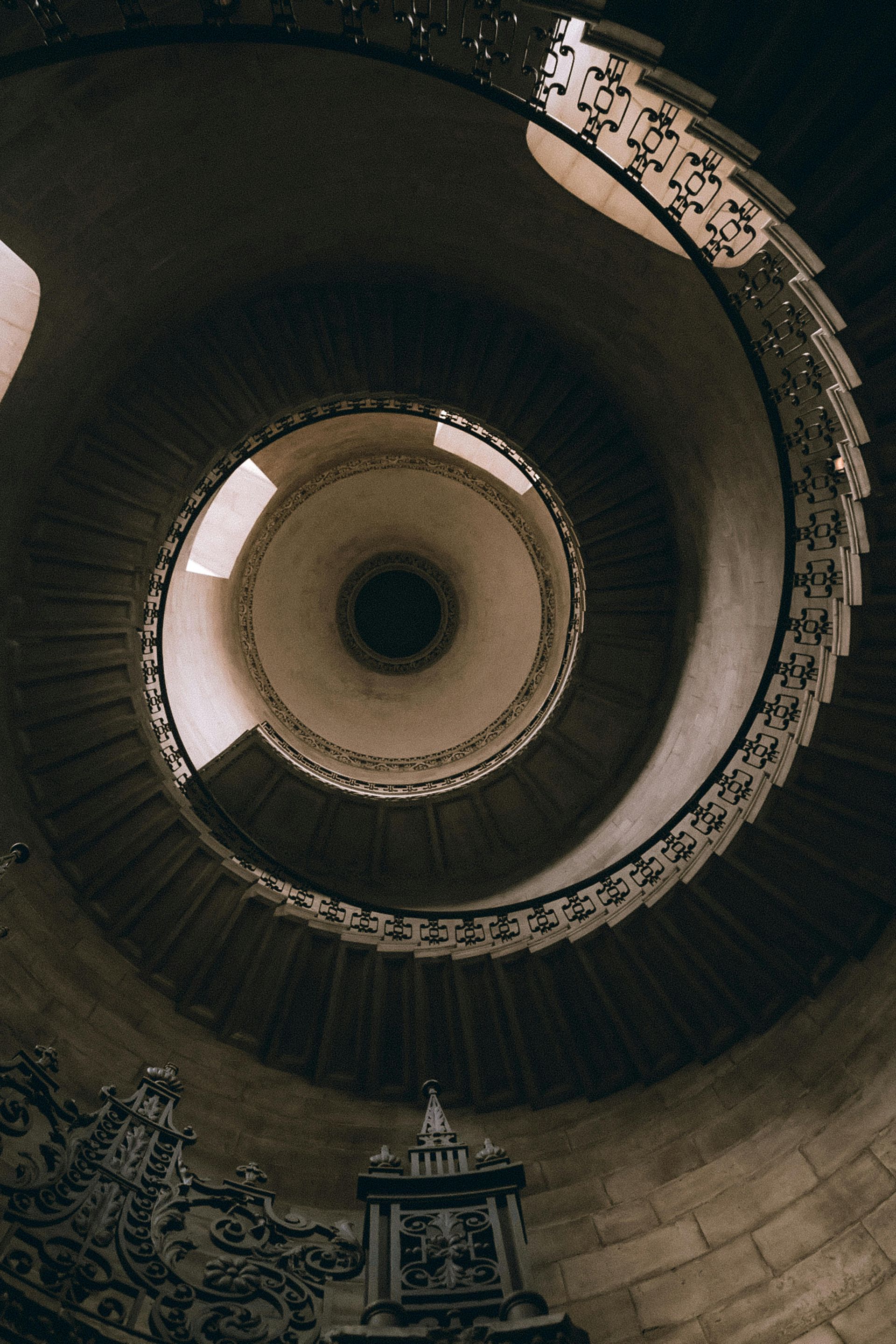 Spiral staircase, ornate railings, ascending towards a central skylight, shot from below.
