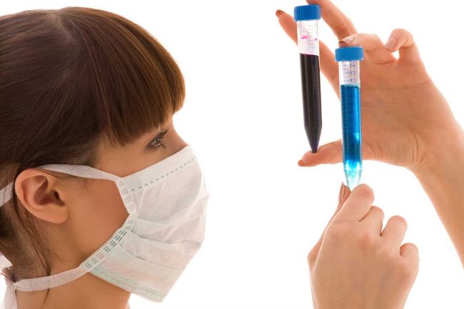 Una mujer con mascarilla examina dos viales, uno negro y otro azul.
