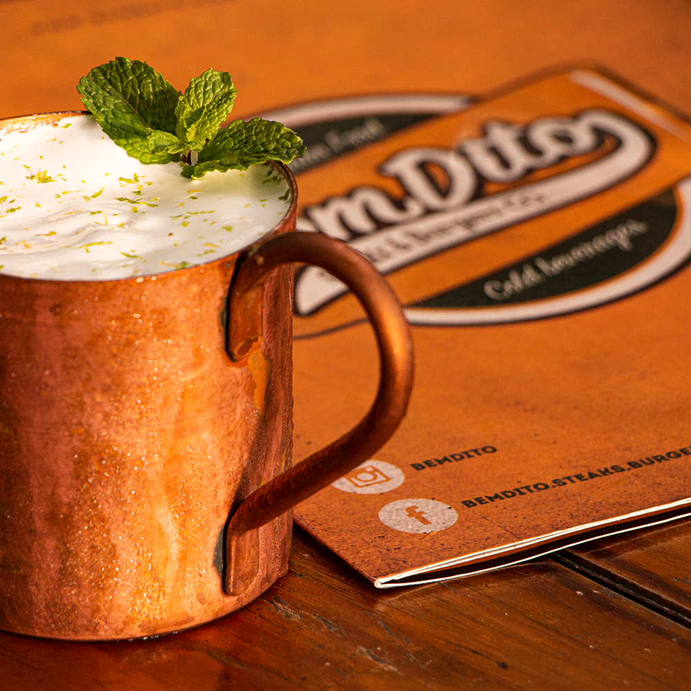 Uma caneca de cobre cheia de uma bebida ao lado de um menu