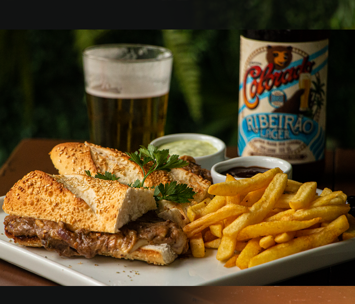 Um sanduíche e batatas fritas em um prato com uma garrafa de cerveja ao fundo.