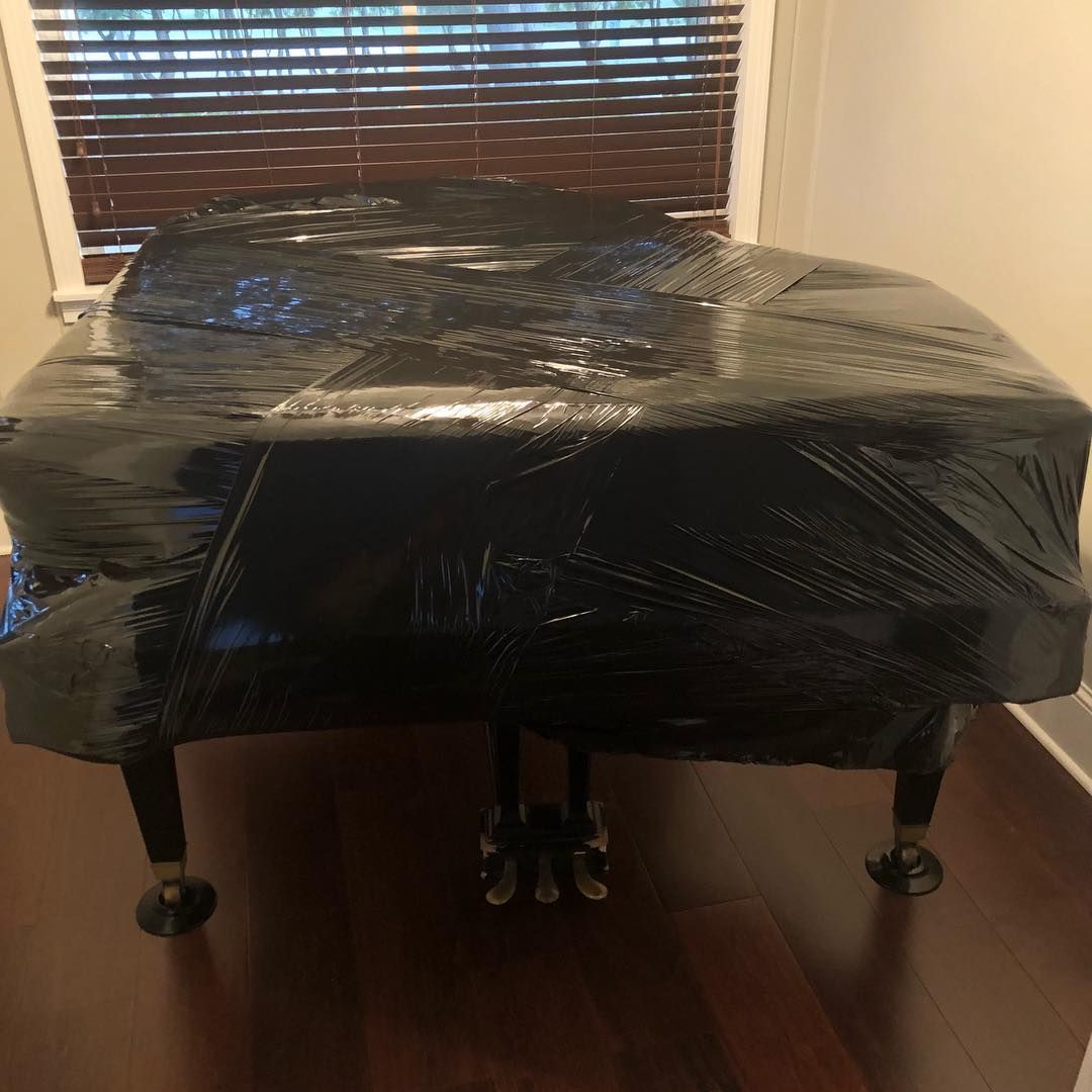 Grand piano wrapped in black plastic, ready for transport.