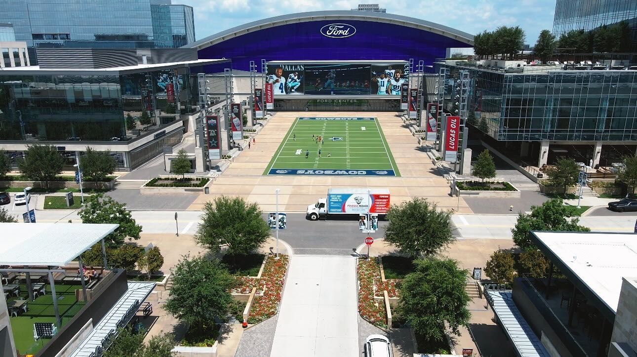 Aerial view of a stadium plaza with a football field setup, surrounded by buildings and landscaping.