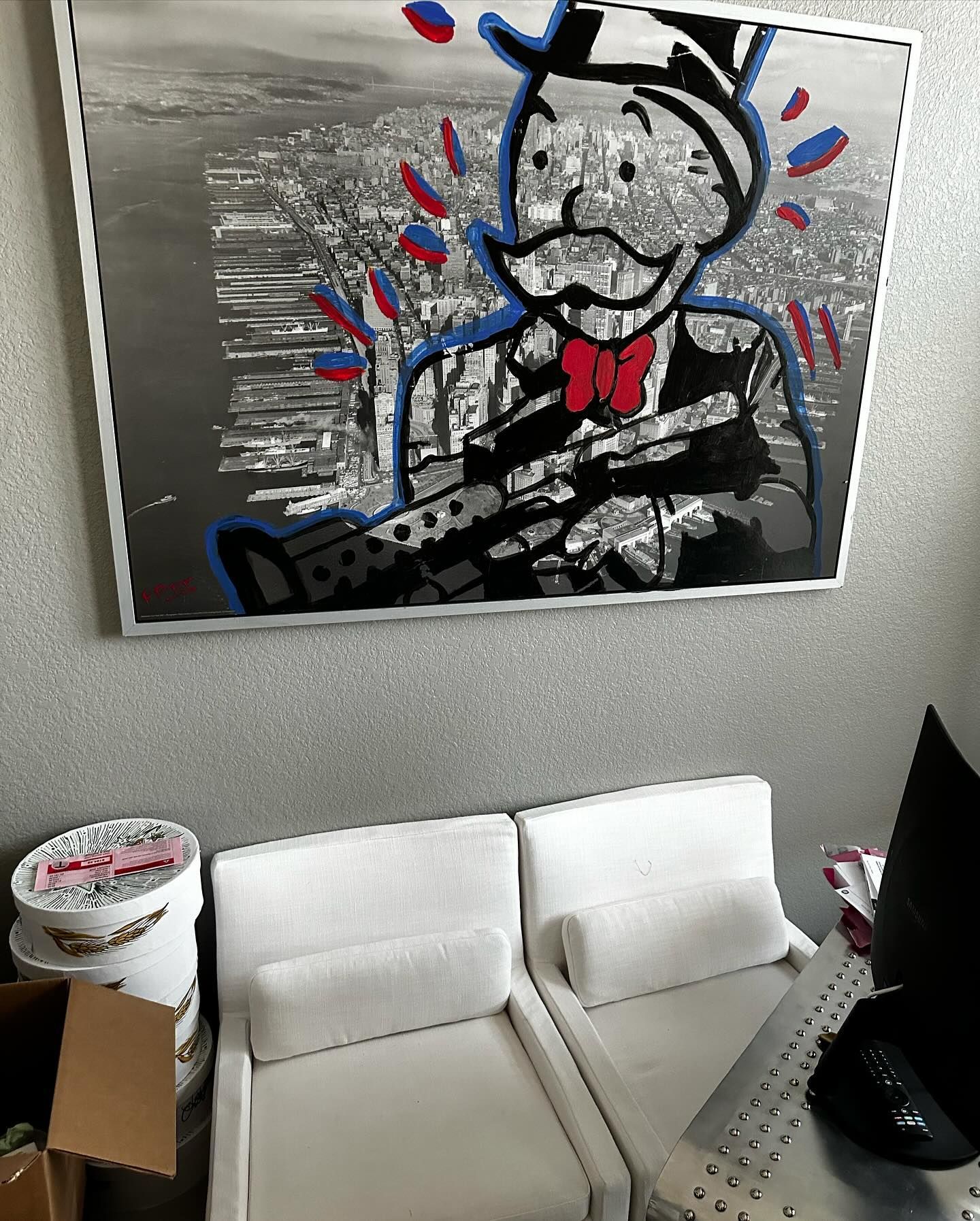 Monopoly Man art with a machine gun, above two white chairs. City backdrop.