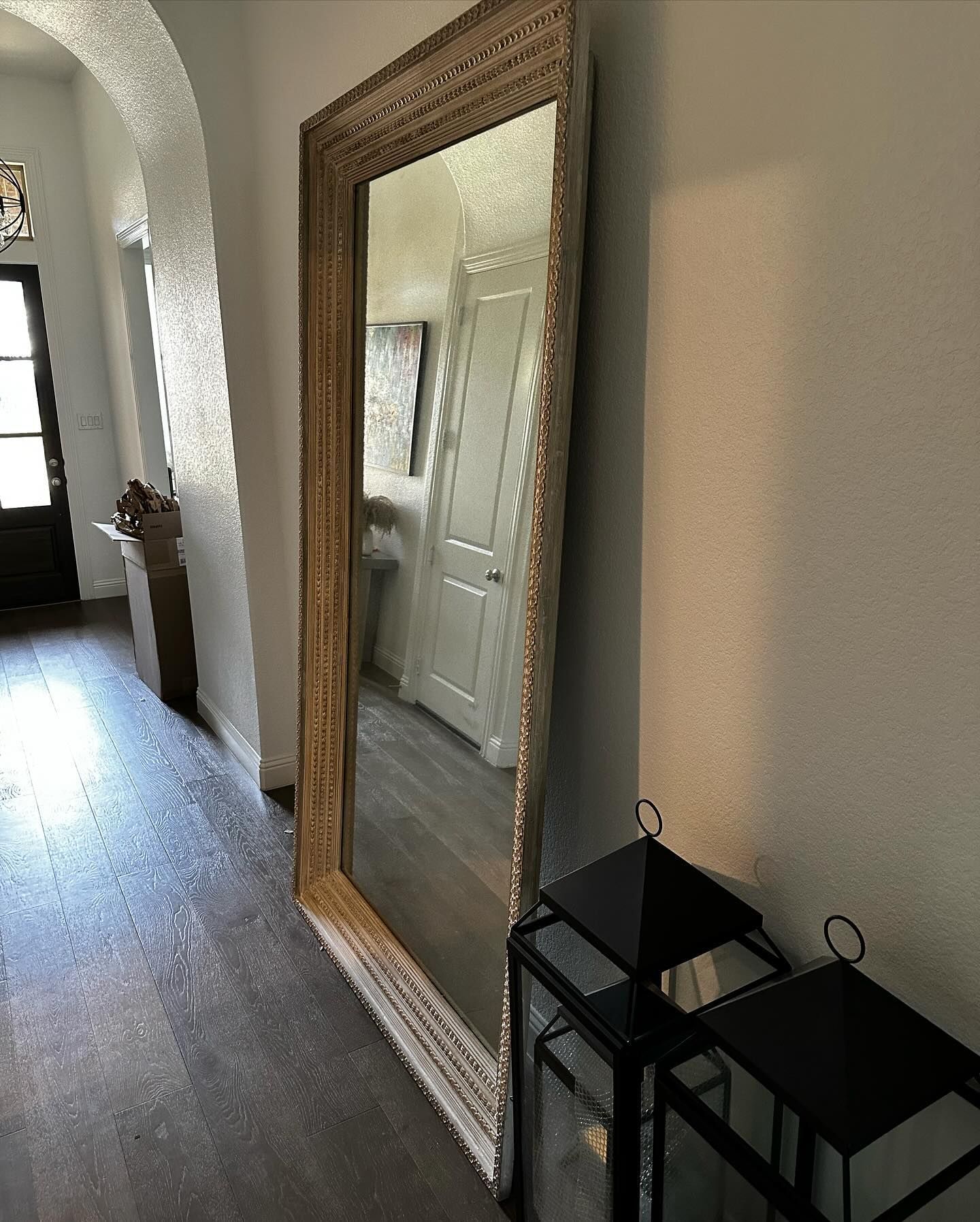 Large ornate framed mirror leaning against a wall, black lanterns in front.