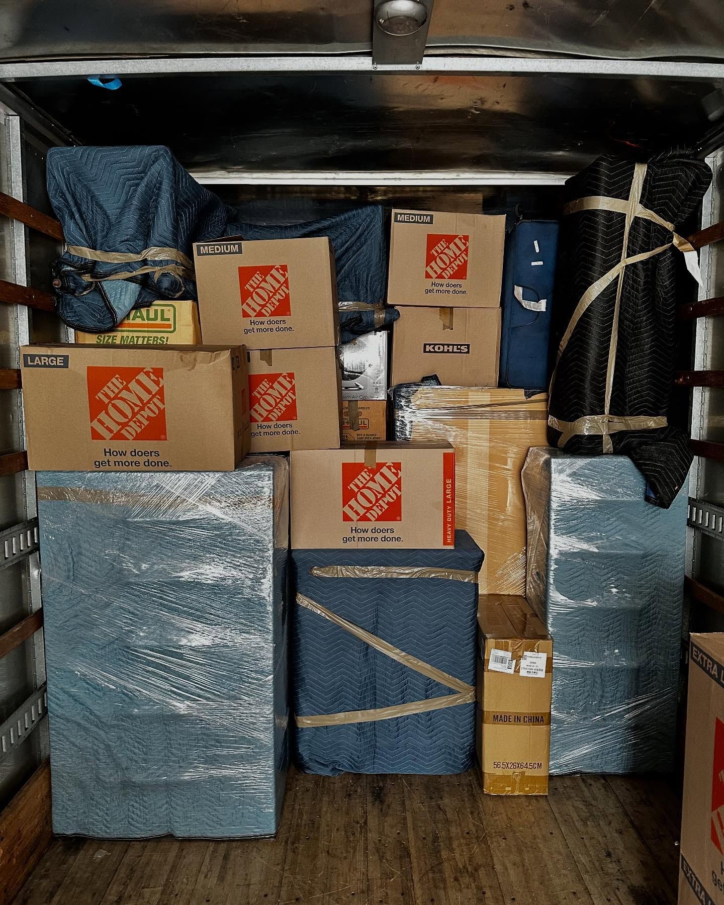 Moving truck interior filled with wrapped furniture and Home Depot boxes.