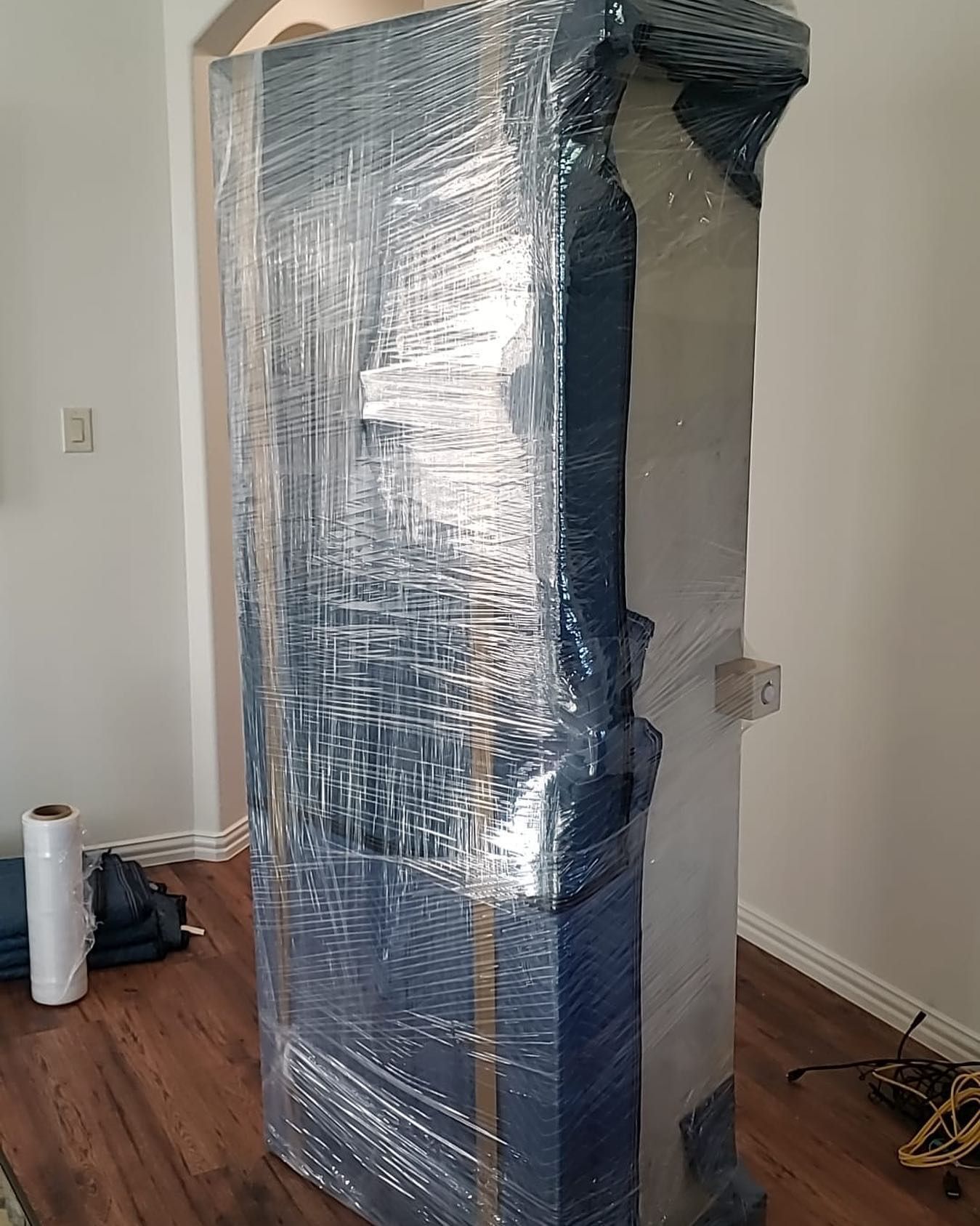 A tall, blue cabinet wrapped in plastic, standing inside a room with hardwood floors.