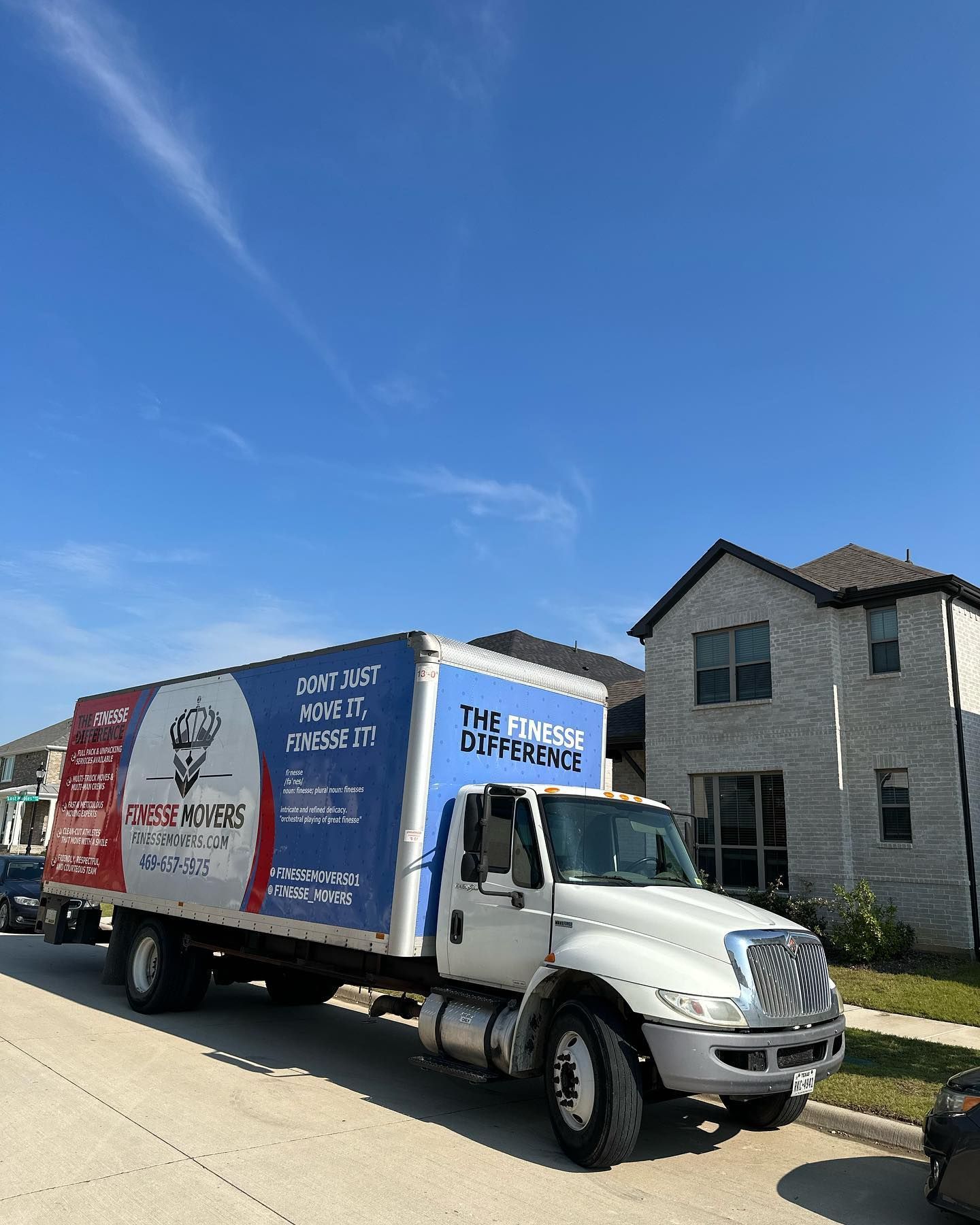 Moving truck parked on a residential street in front of a house on a sunny day.