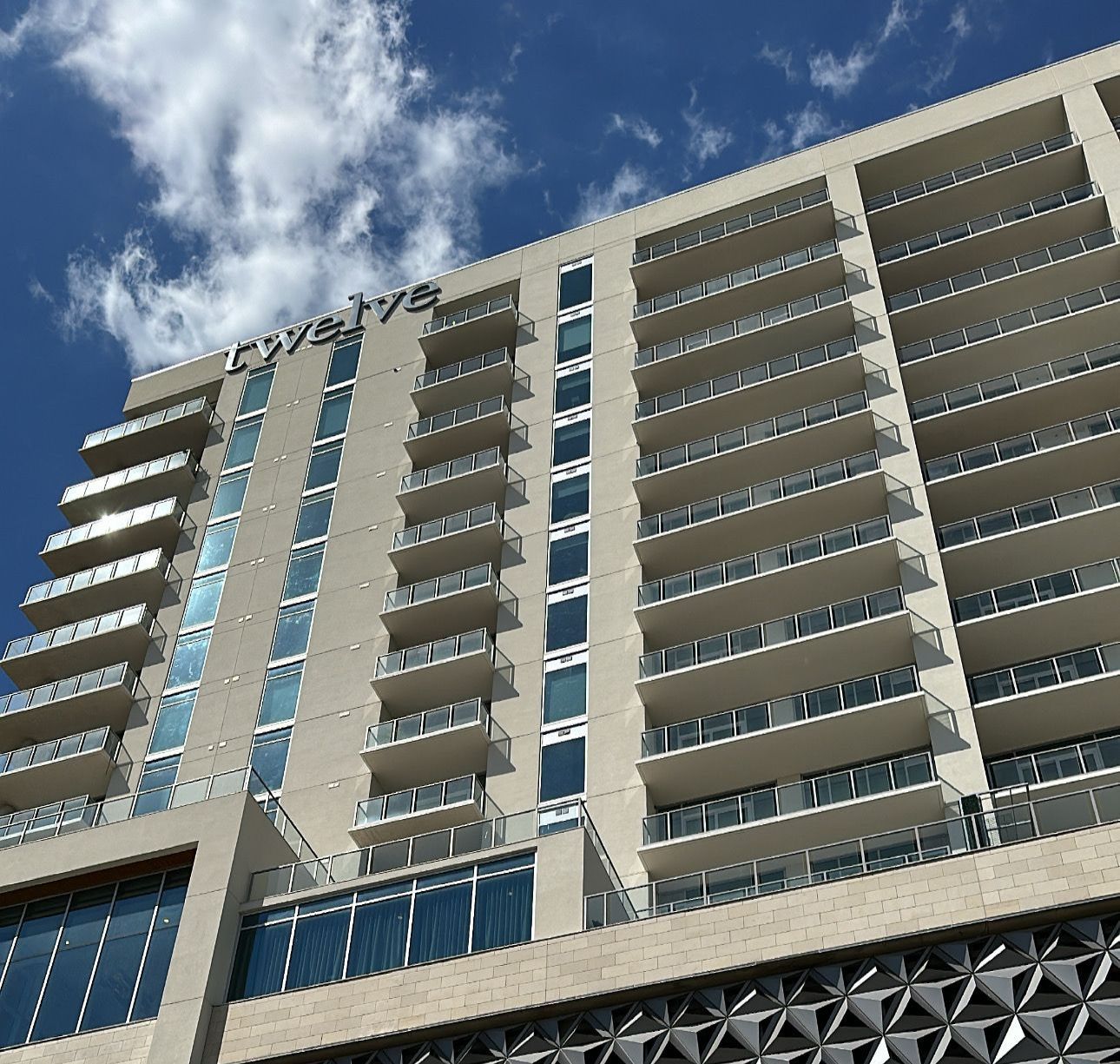 Woman in dark green uniform smiles, holding papers, amidst indoor plants.