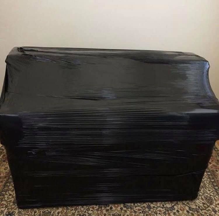 Black sofa tightly wrapped in black plastic, ready for moving.