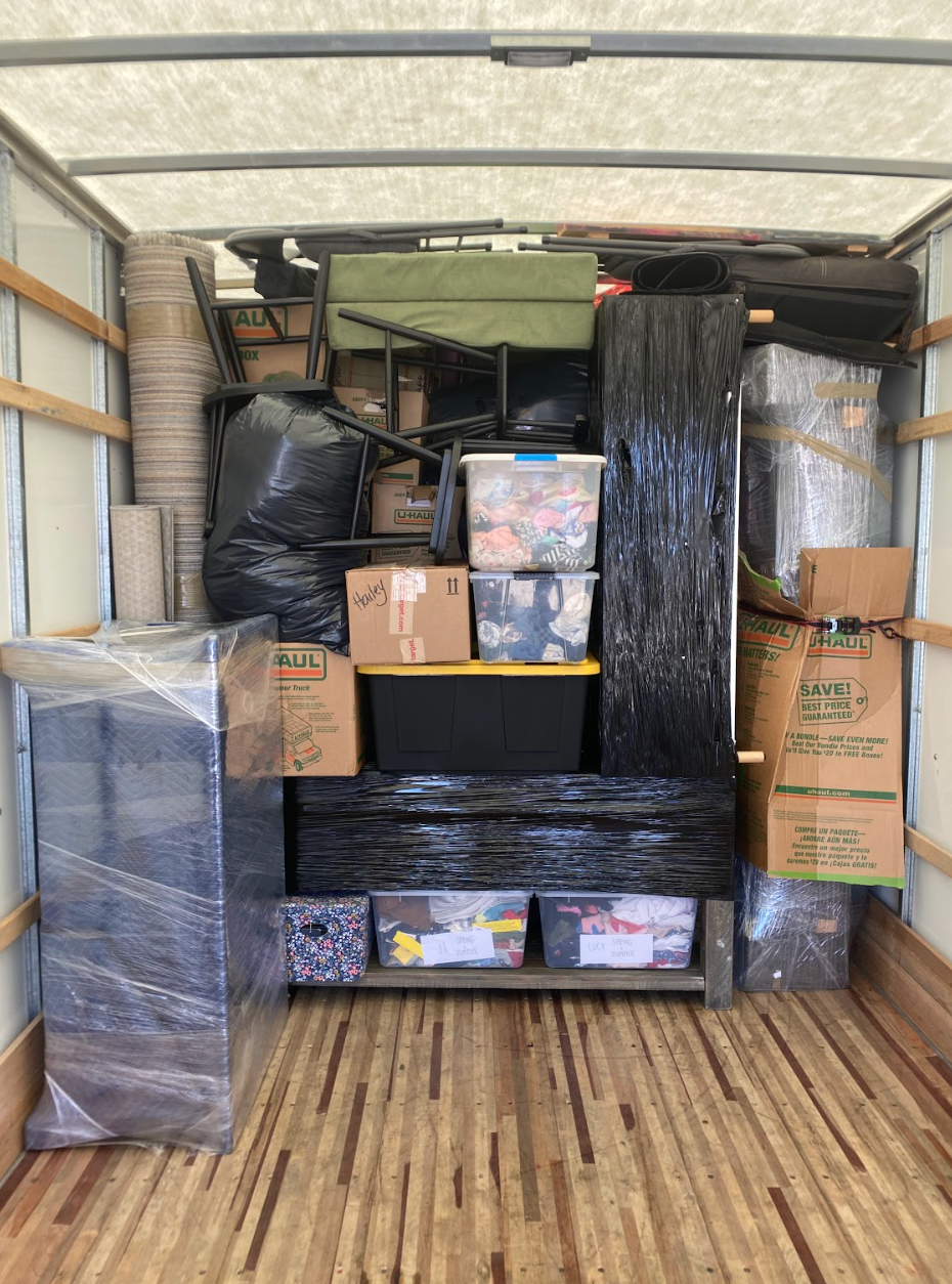 Woman in dark green uniform smiles, holding papers, amidst indoor plants.
