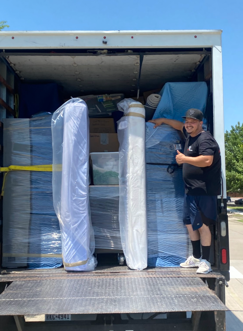 Woman in dark green uniform smiles, holding papers, amidst indoor plants.