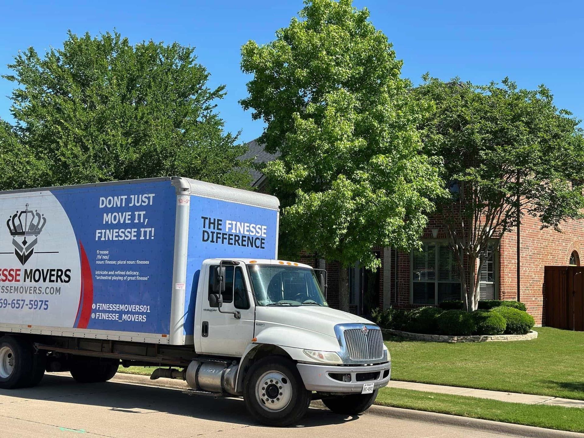 Moving truck parked in front of a house. The truck has blue and white branding with 