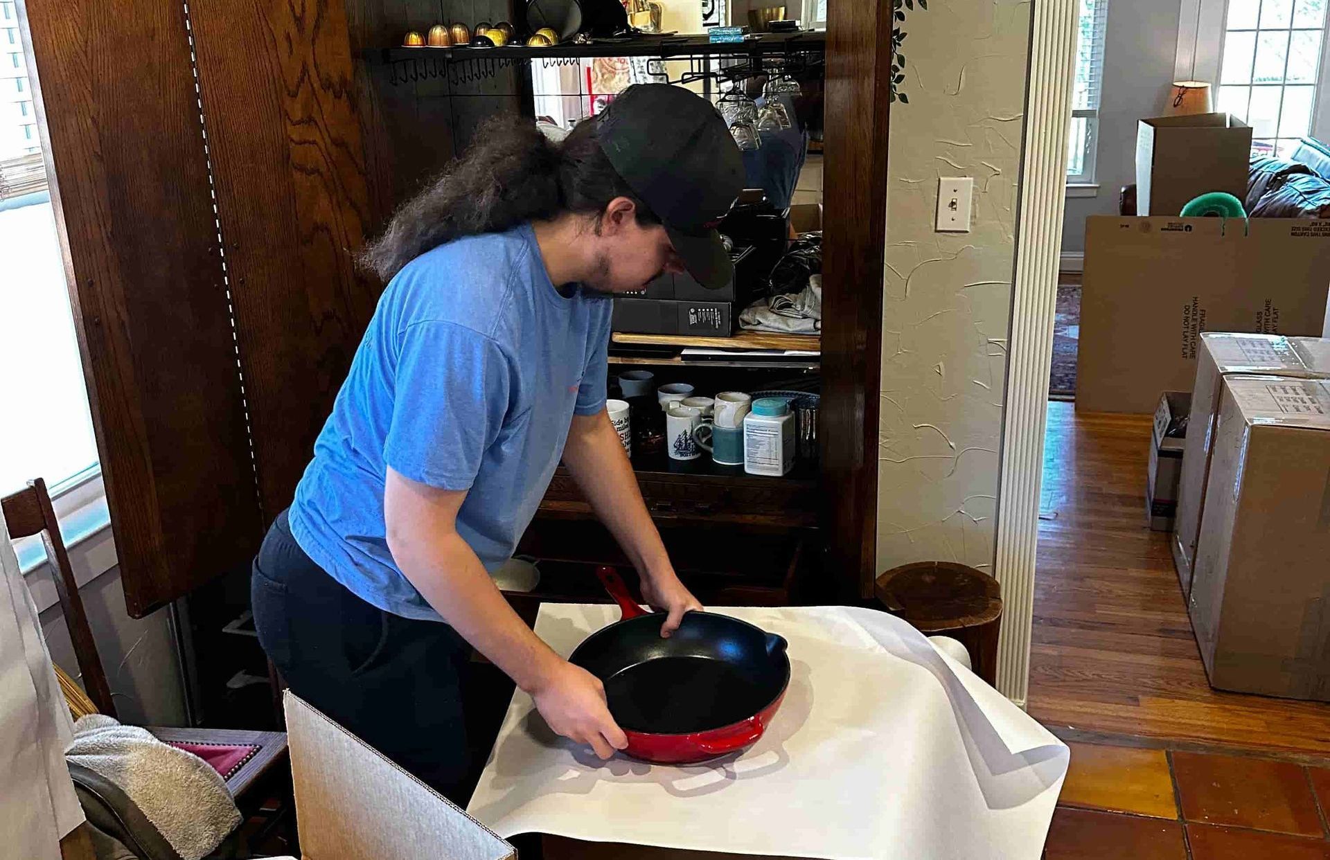 Person in a blue shirt wrapping a red and black pot on a table, with a wooden cabinet in the background.