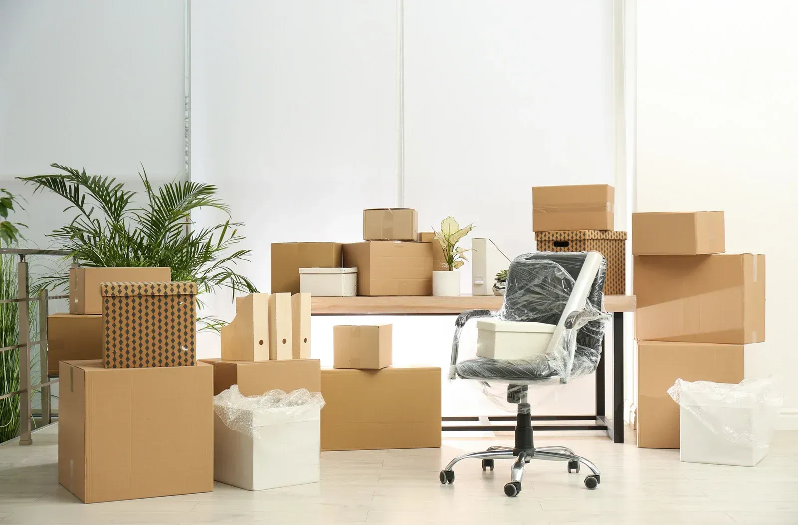 Office space with cardboard boxes, a desk, and a chair wrapped in plastic, indicating a move.