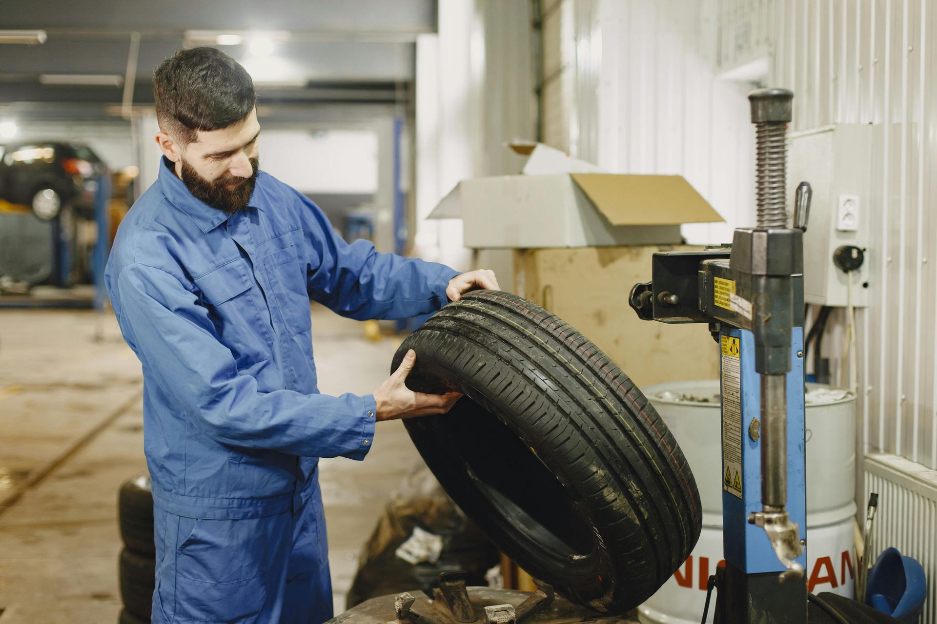 Mechanic in blue coveralls examines a tire in a garage, next to tire changing machine.