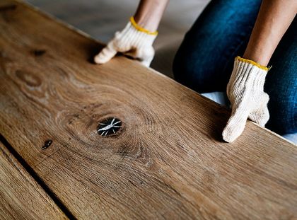 Une personne portant des gants installe un parquet.