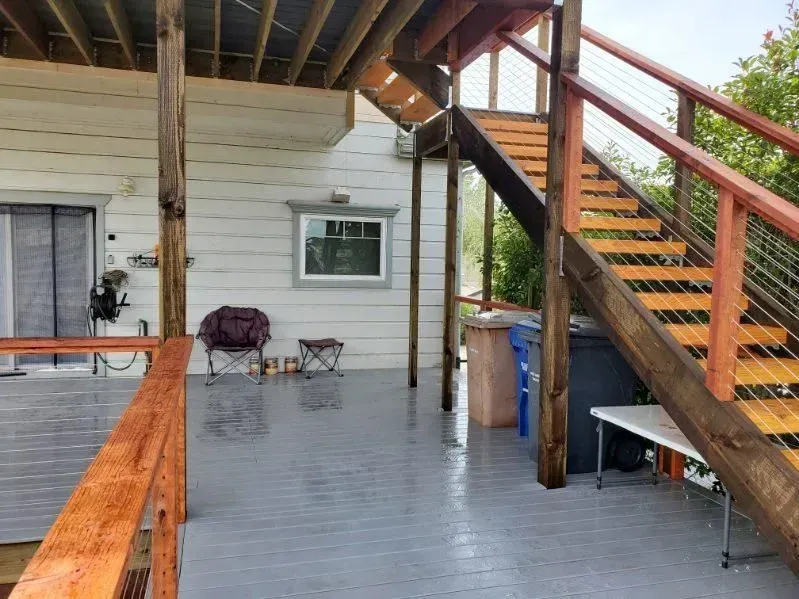 Wooden deck and stairs. Gray painted floor, light-colored siding, and a window.