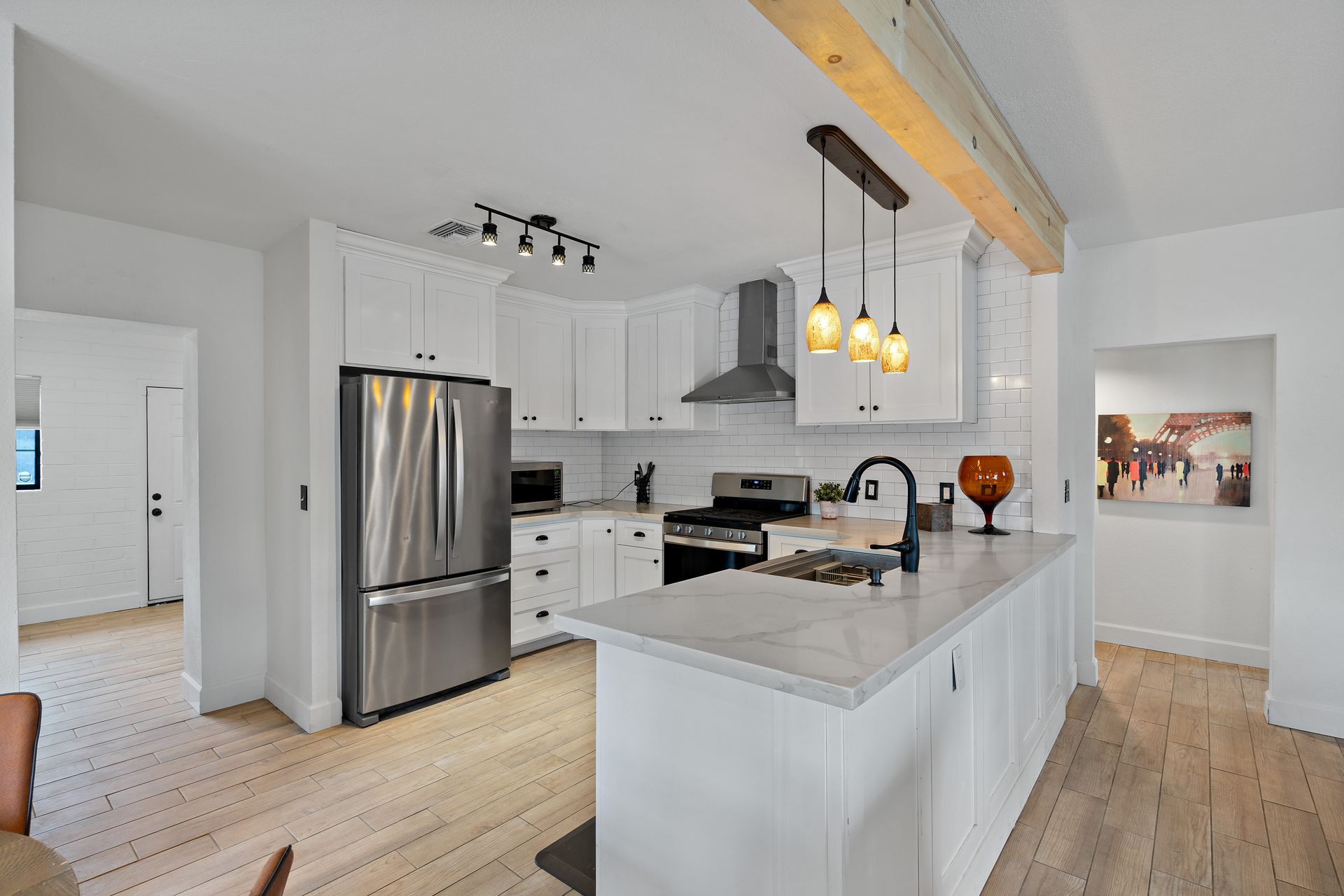 White kitchen with stainless steel appliances, marble island, and wooden beams.