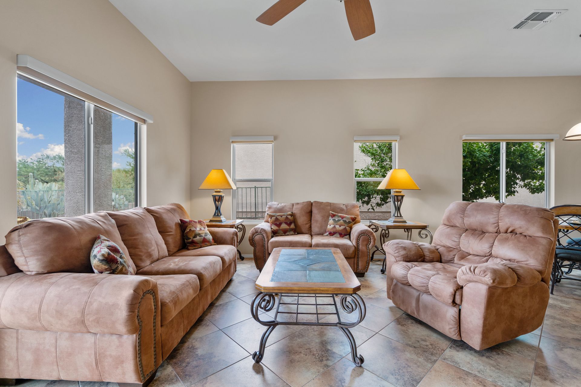 Living room with brown furniture, including sofa, loveseat, and recliner. Beige walls, large windows, and a ceiling fan.